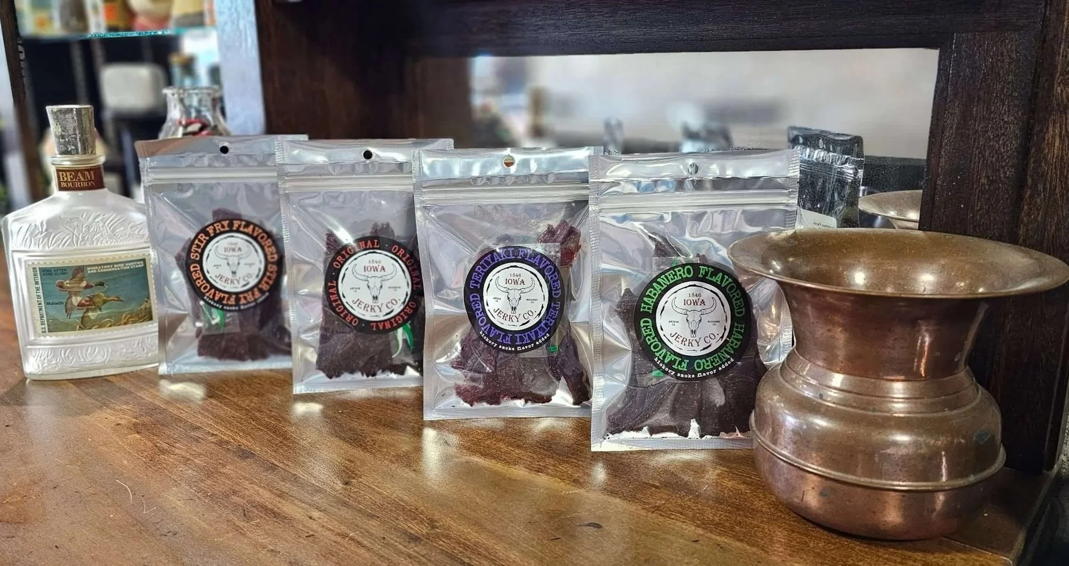 Various packages of beef jerky on a wooden surface, with a copper vessel and a stone bowl nearby.