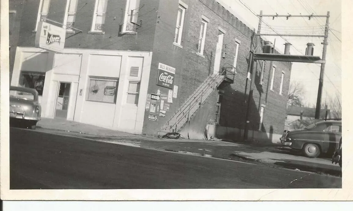 Street scene with a brick building, parked cars, and utility poles.