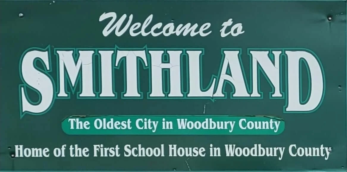 Welcome sign for Smithland, the oldest city in Woodbury County, referencing the first school house.