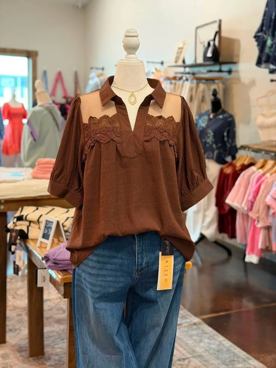 A mannequin dressed in a brown top with lace details and blue jeans inside a clothing store.