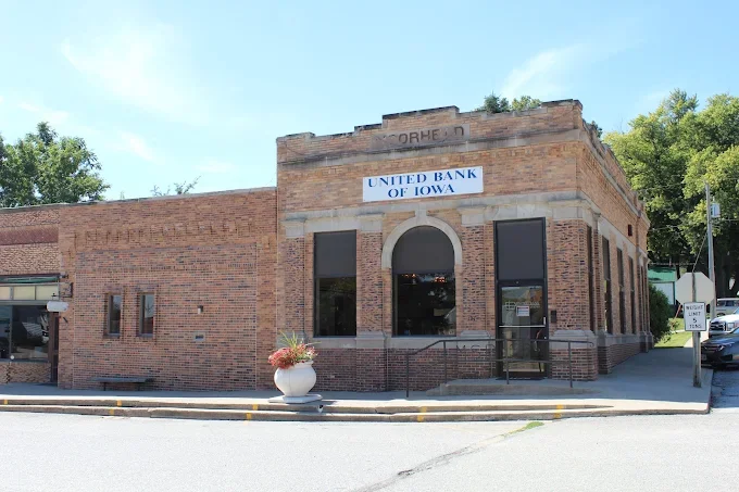 Brick building with a sign that reads 'United Bank of Iowa,' located on a city street with a sidewalk and cars parked nearby.