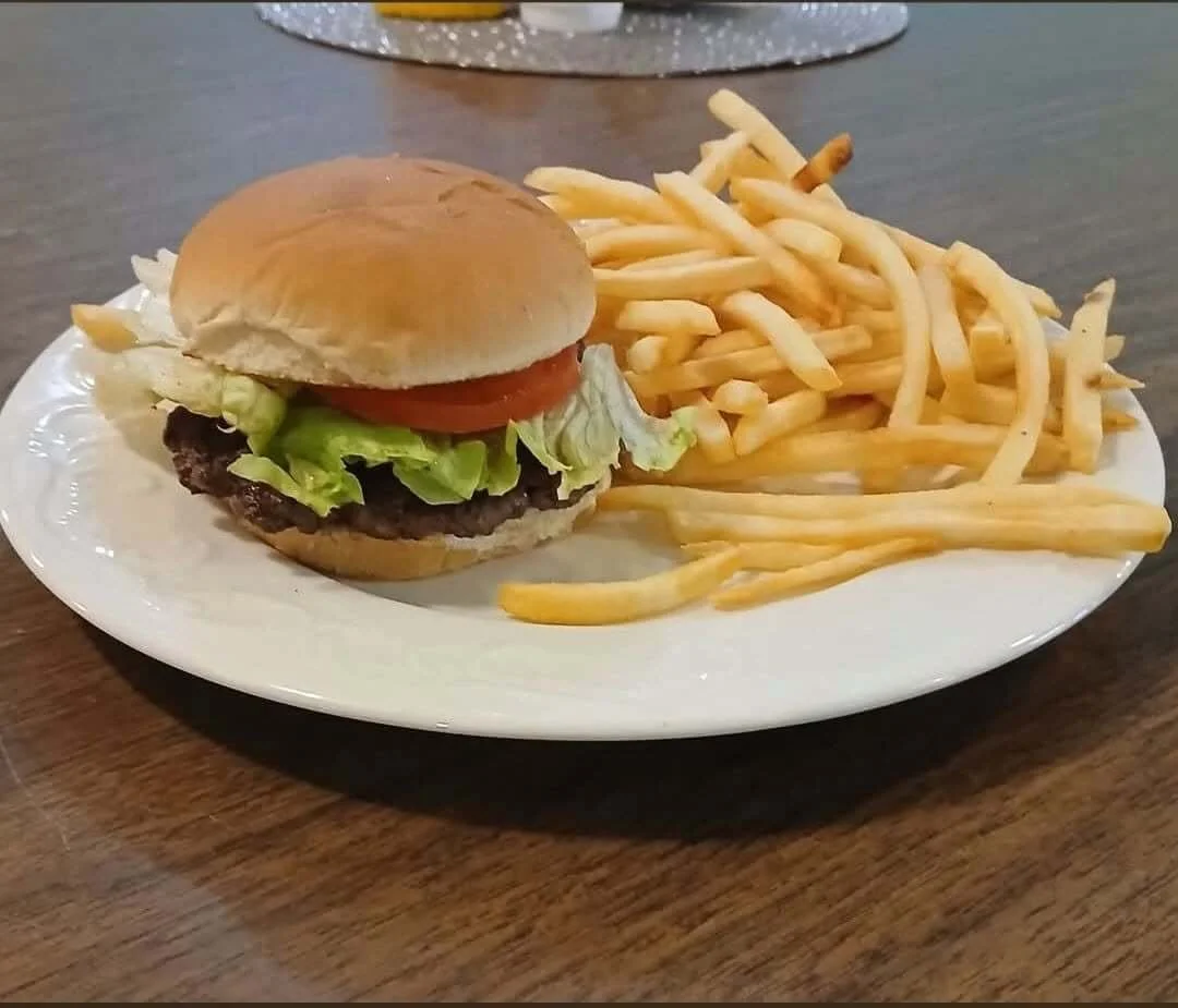 A plate of food with a cheeseburger, French fries, and a glass of iced tea on a wooden table.