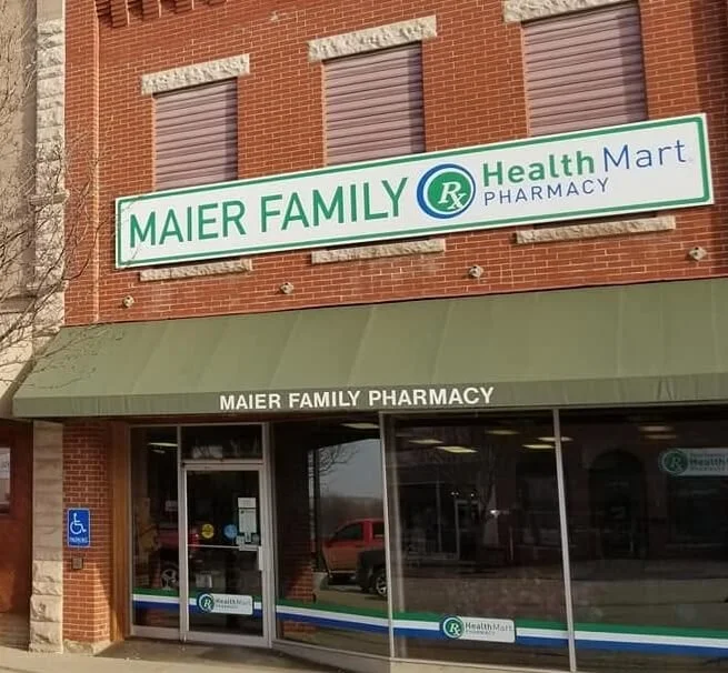 Storefront of Maier Family Pharmacy with green awning and large sign reading Maier Family Health Mart Pharmacy, featuring a green and blue health-related logo.