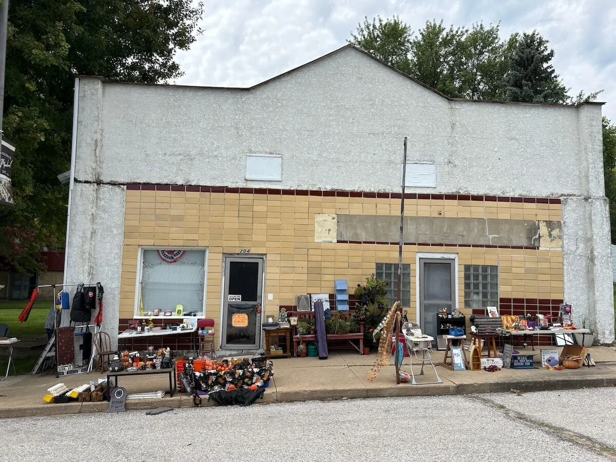 Exterior of a building with items for sale displayed outside, including halloween decorations, furniture, and miscellaneous household items.