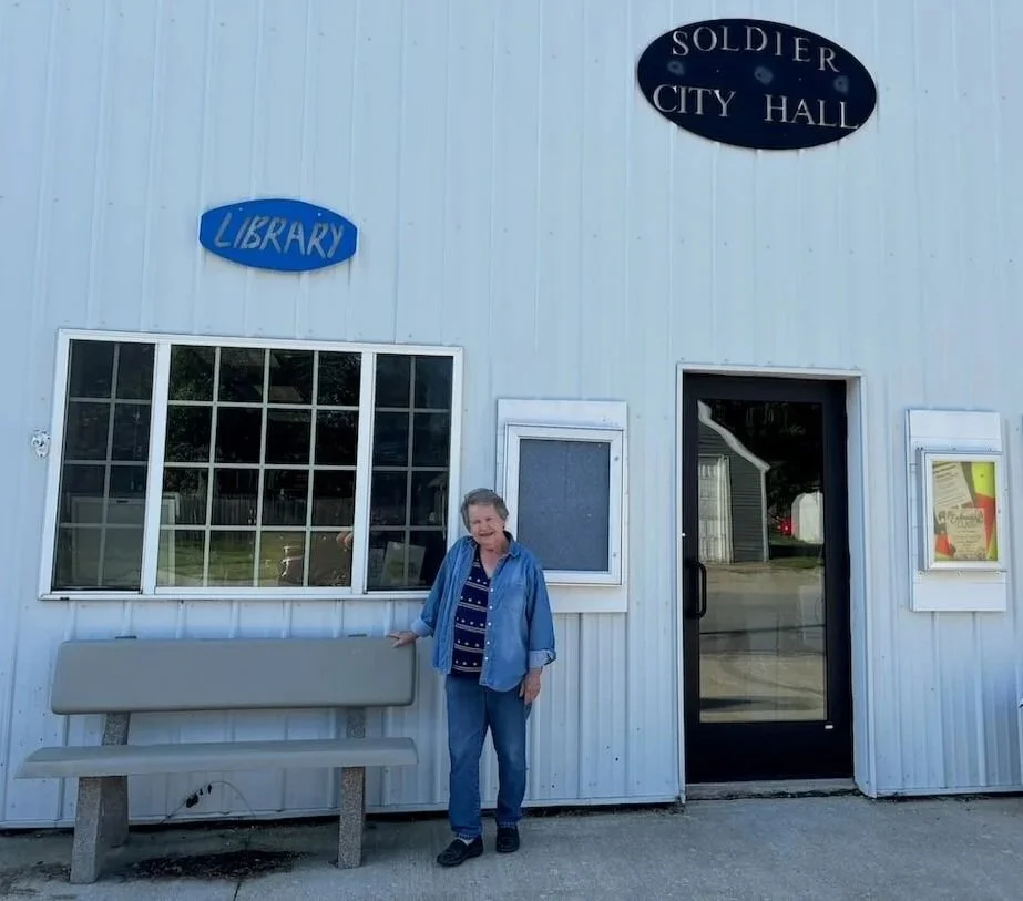A smiling woman standing outside of a white building labeled 'Soldier City Hall' and 'Library'.