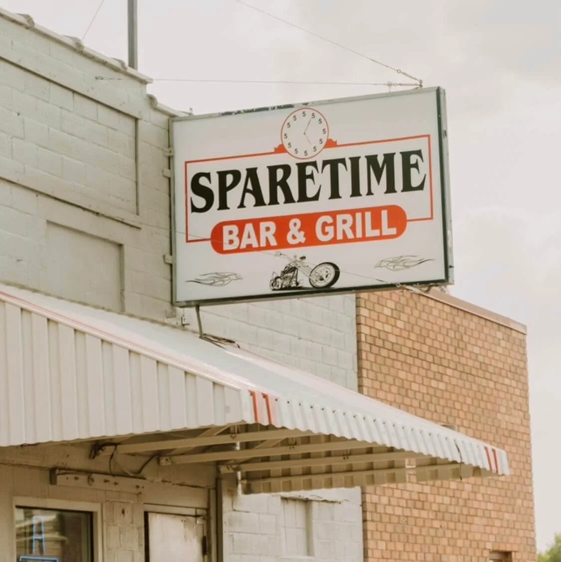 Sign for SparetTime Bar and Grill with a clock, motorcycle graphic, and flames design.