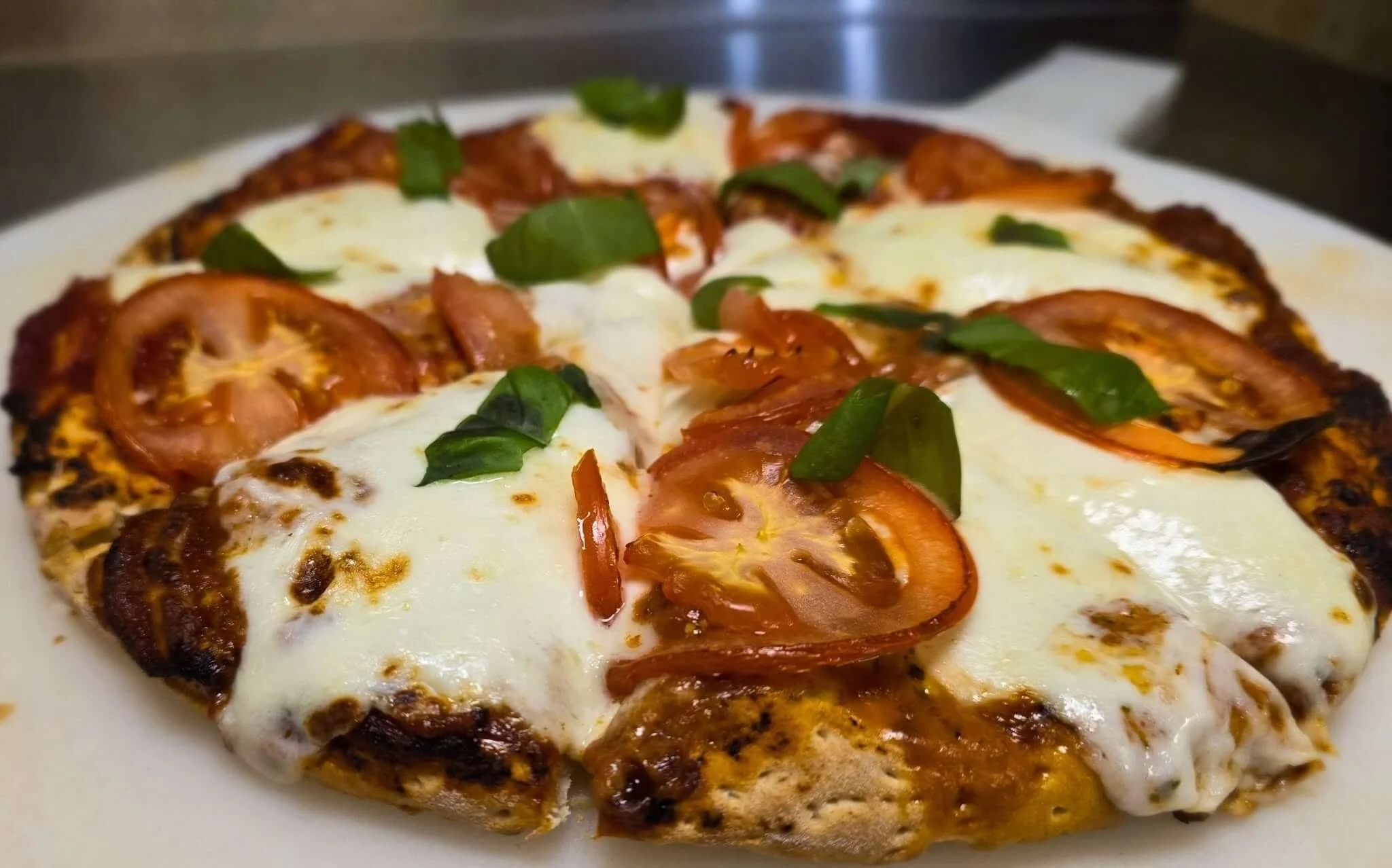 Close-up of a homemade pizza topped with fresh basil, sliced tomatoes, melted cheese, and seasoned crust.