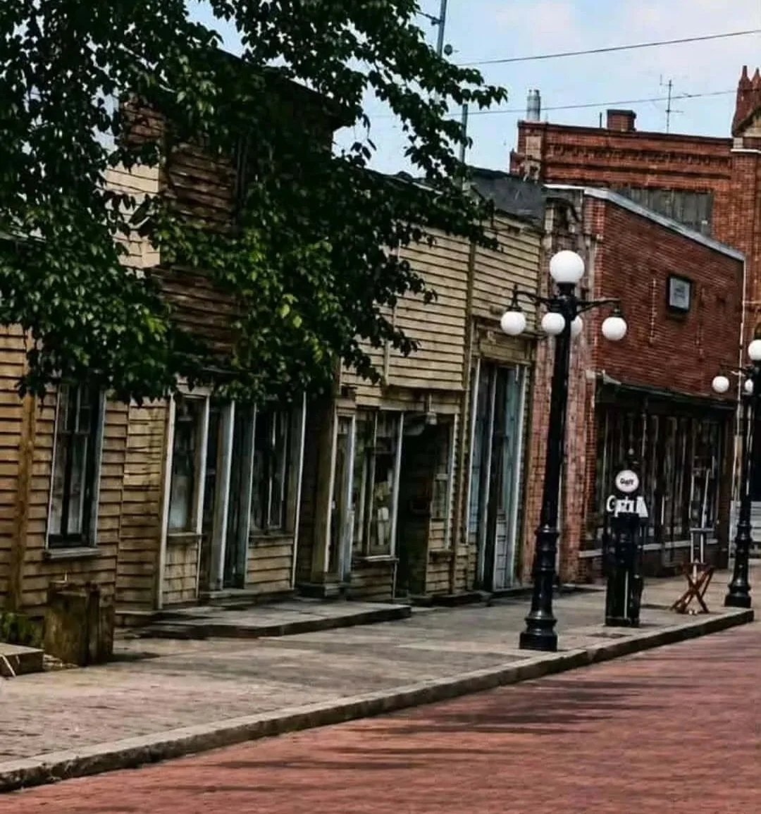 Sandy brick building with brick sidewalk, trees and black lightpole in front.