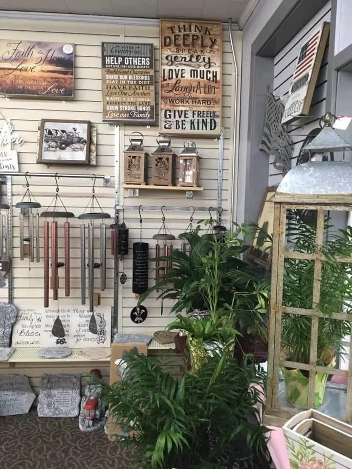 Home decor and gardening store display with wind chimes, inspirational signs, lanterns, and potted plants.