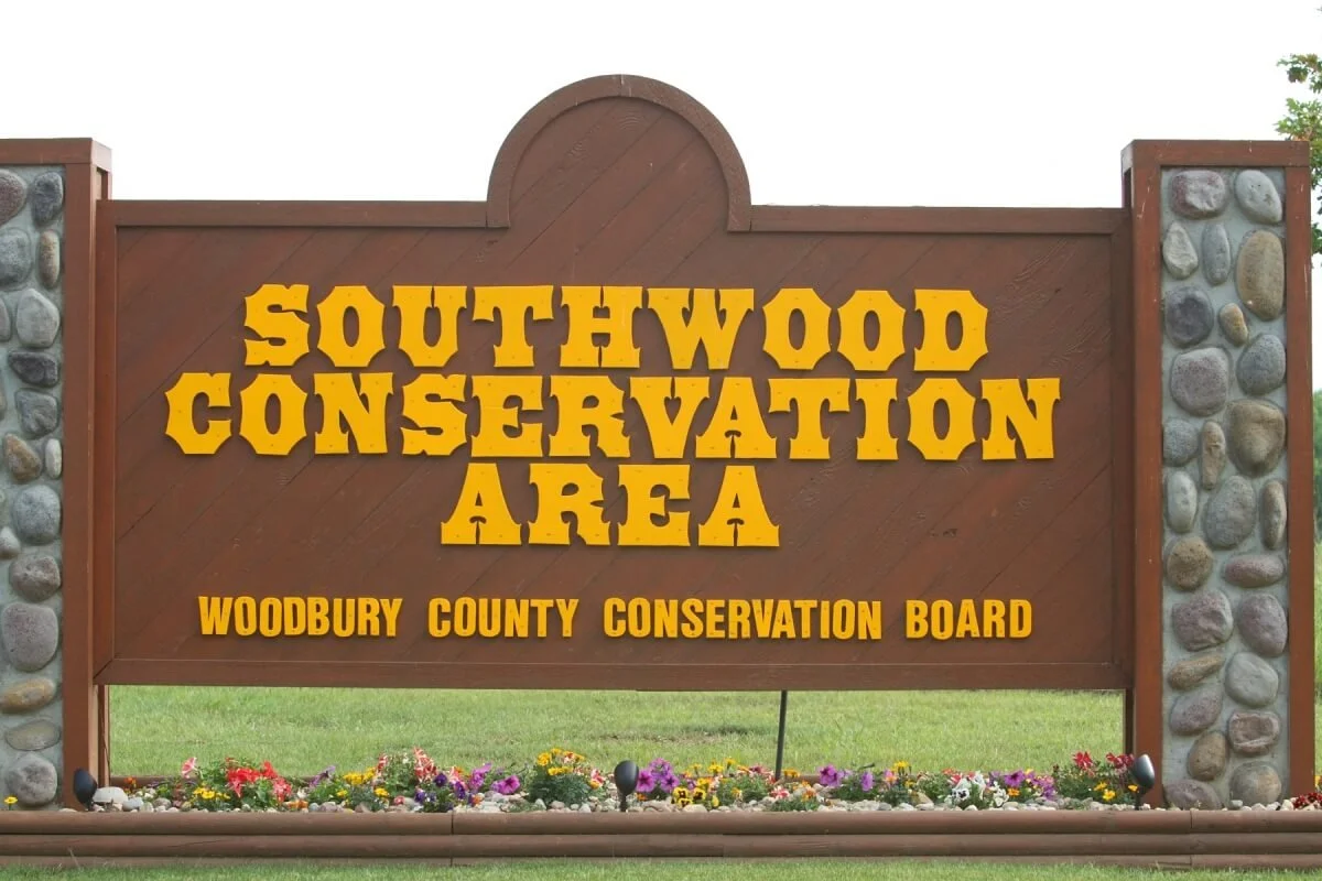 Sign reading 'Southwood Conservation Area, Woodbury County Conservation Board' with a flower bed at the base.