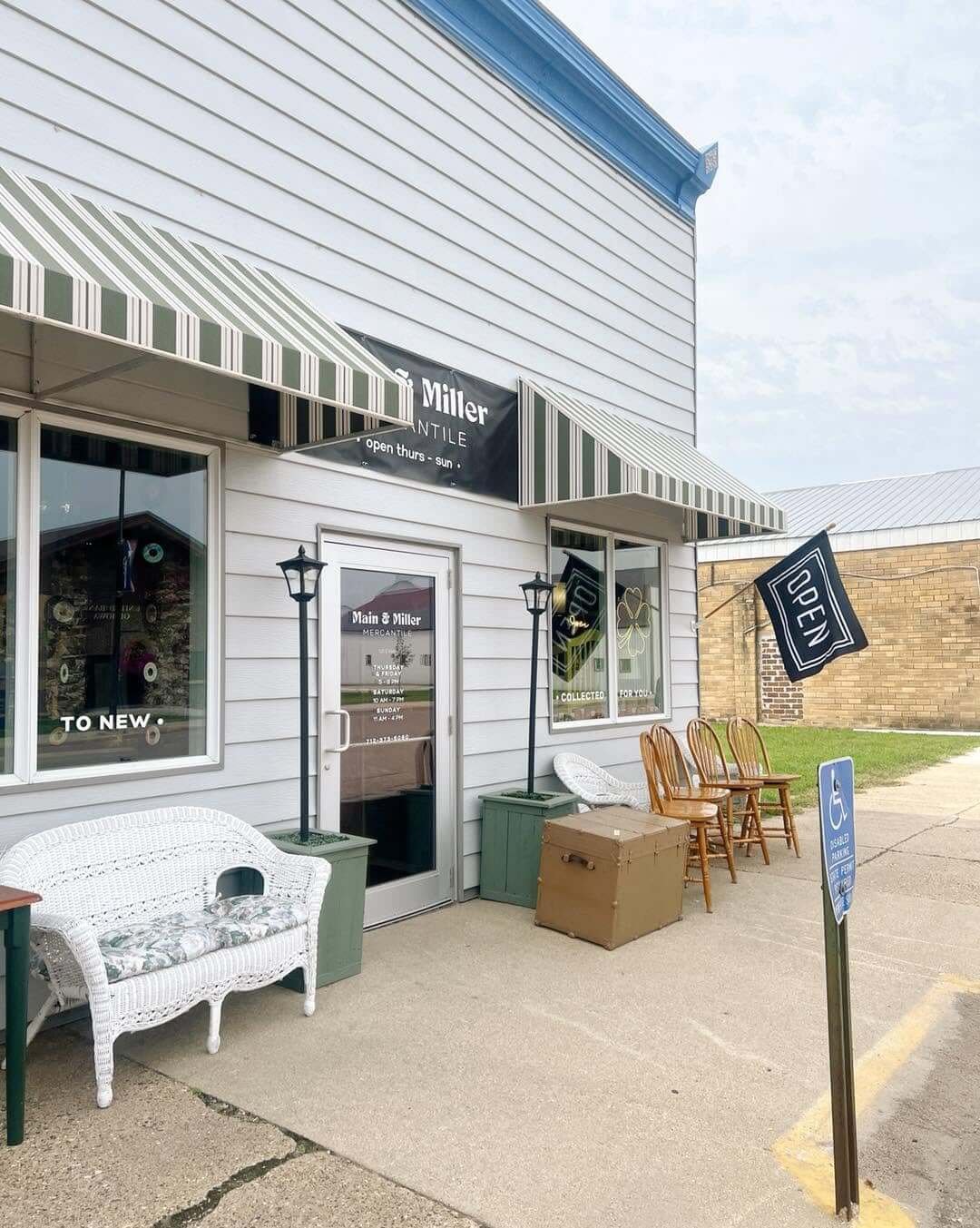 Exterior of a small shop with a white building, striped awnings, outdoor seating, a Starbucks sign, and a handicap parking sign.