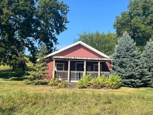 A red house with a porch surrounded by trees and green grass.