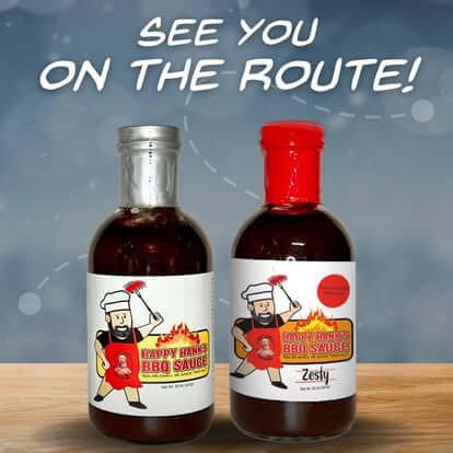 Two bottles of barbecue sauce with cartoon chef labels; one with a silver cap and the other with a red cap, on a wooden surface against a blue background with the text "See you on the route!"
