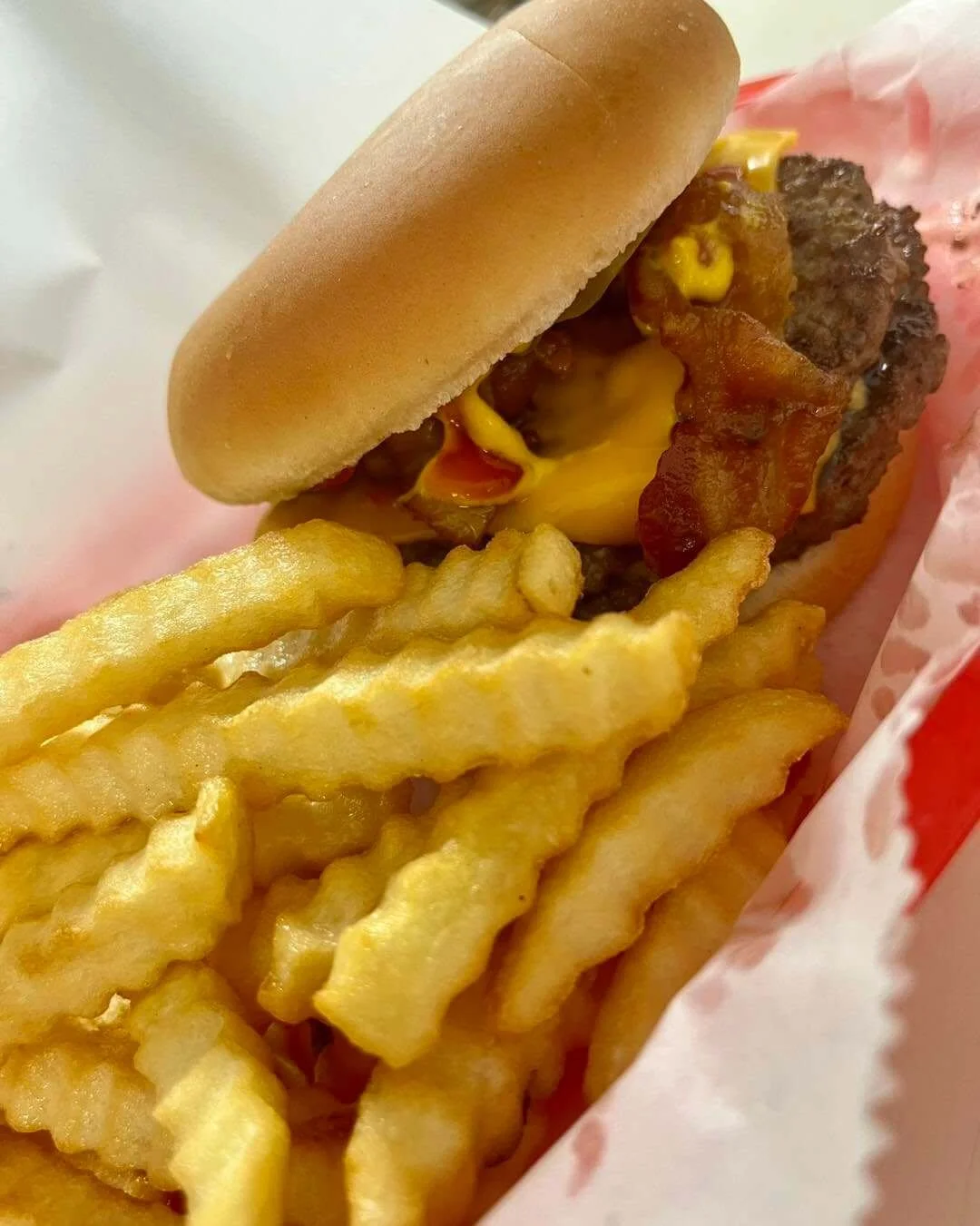 A cheeseburger with bacon, topped with mustard and ketchup, served with crinkle-cut fries.