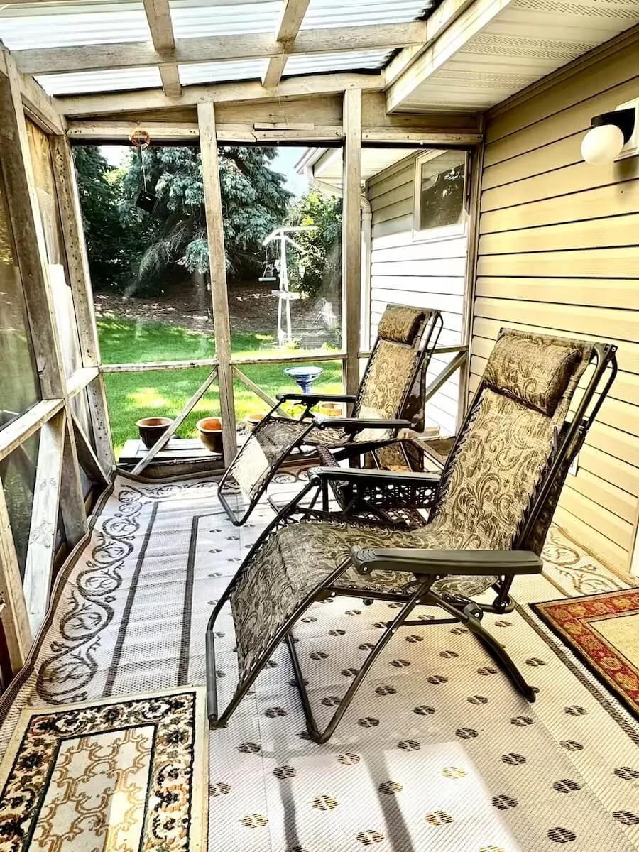 Enclosed porch with chairs and a view of a grassy backyard with trees and a swing set.