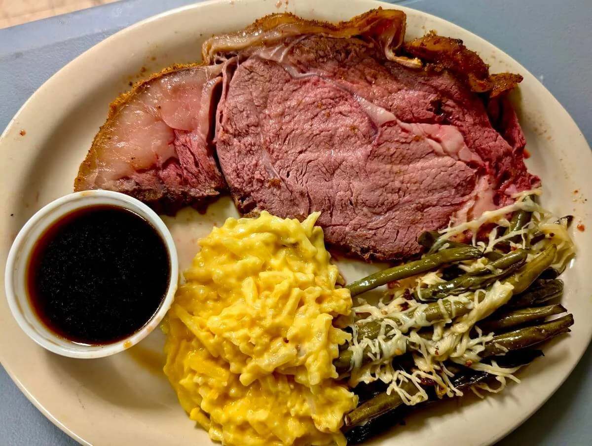 A plate with slices of roast beef, scrambled eggs, cooked green beans, and a small bowl of dark gravy.
