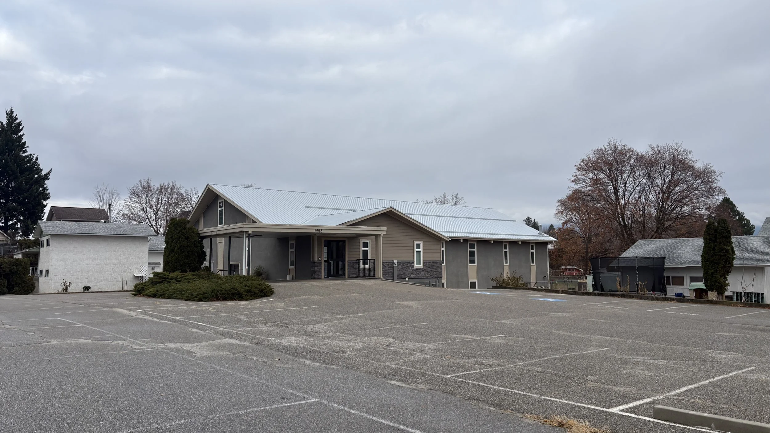 A parking lot with marked spaces in front of several modern houses, including one with solar panels on the roof, under a cloudy sky.