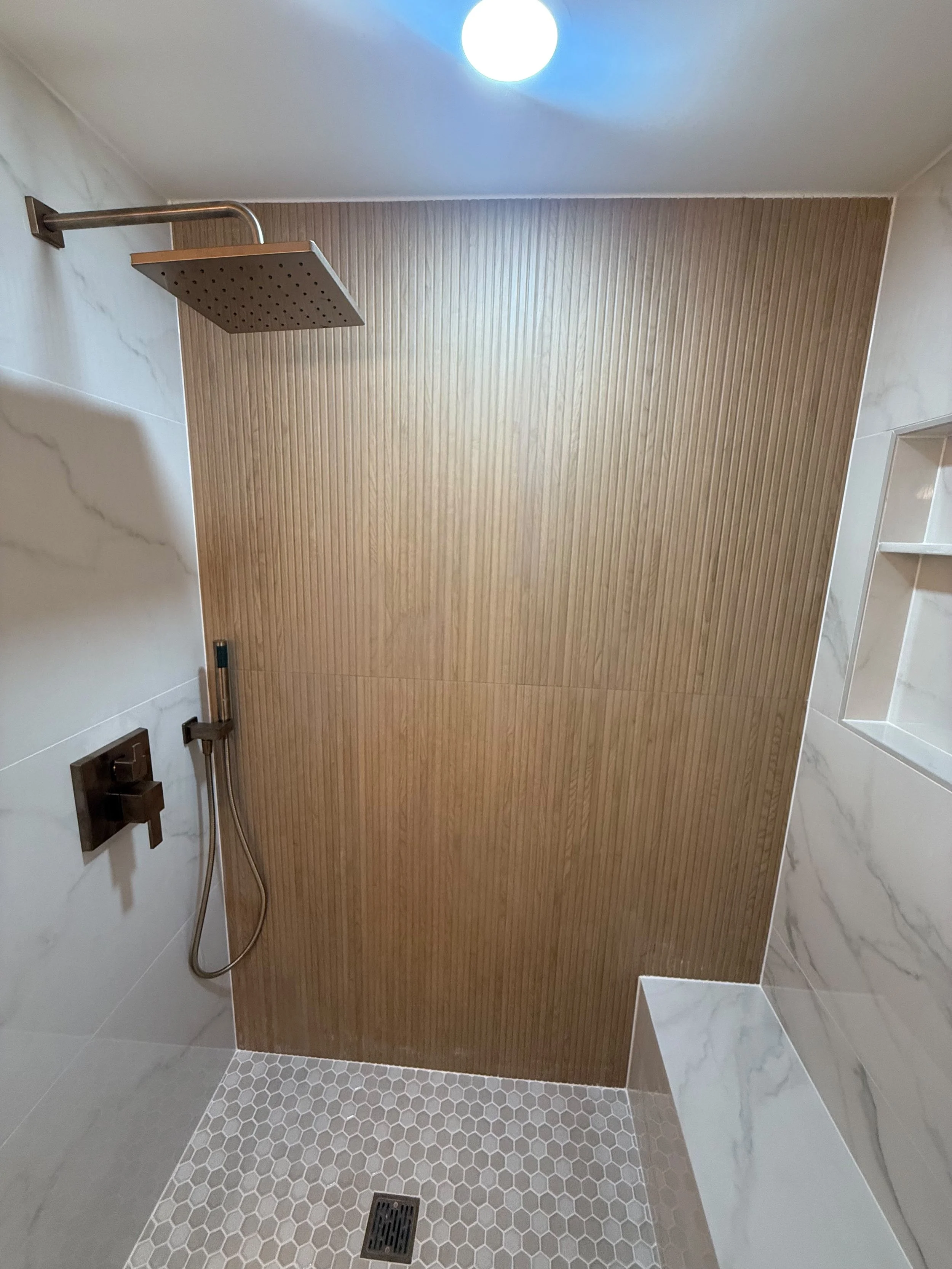 Custom walk-in shower with large- format wood-look tile, matte black shower fixtures, built-in bench, and premium bathroom renovation in Rochester, MI.