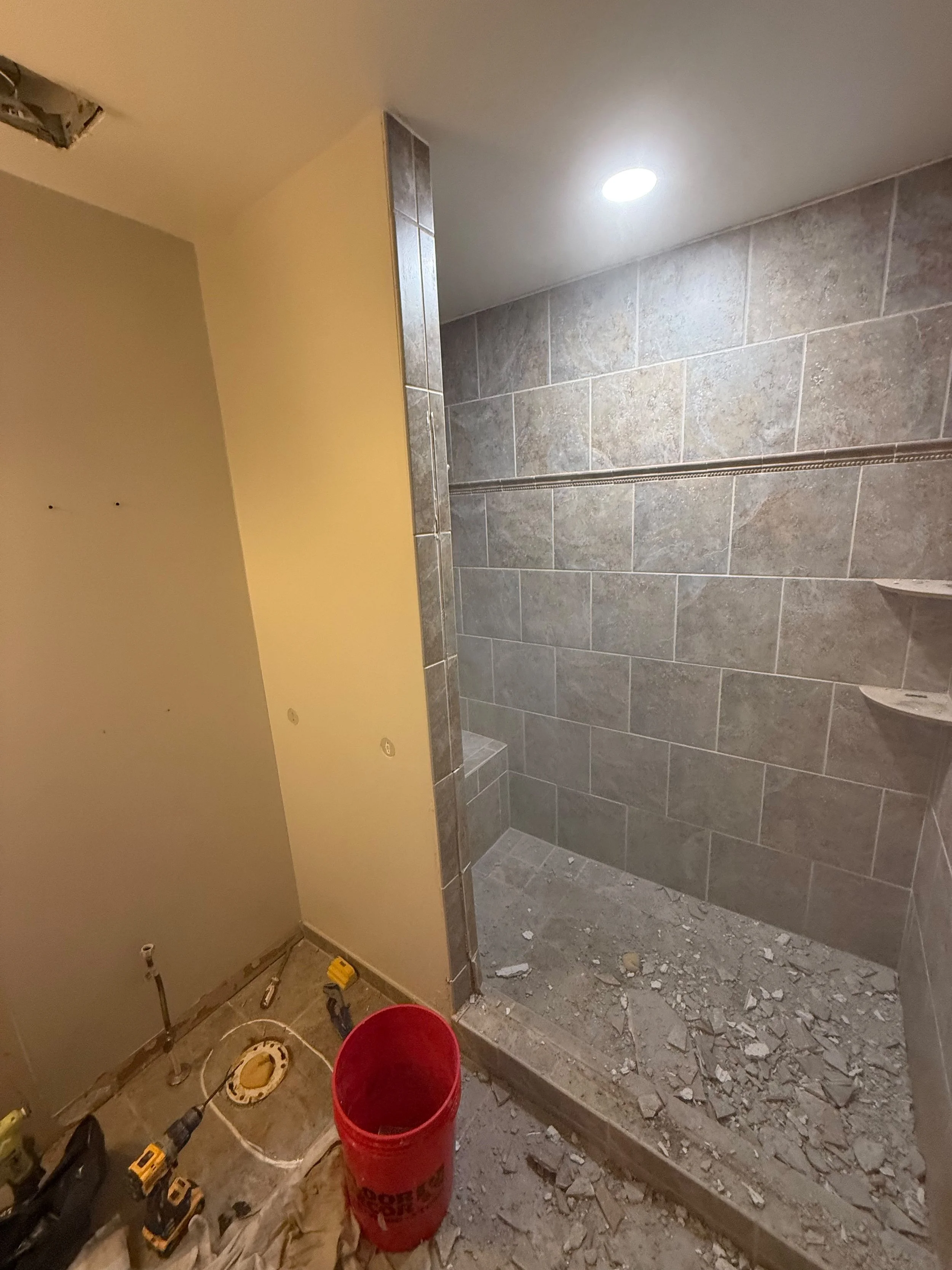 Walk-in shower during a bathroom renovation featuring large-format gray wall tile, a built-in bench, and waterproof shower installation in Rochester, MI.