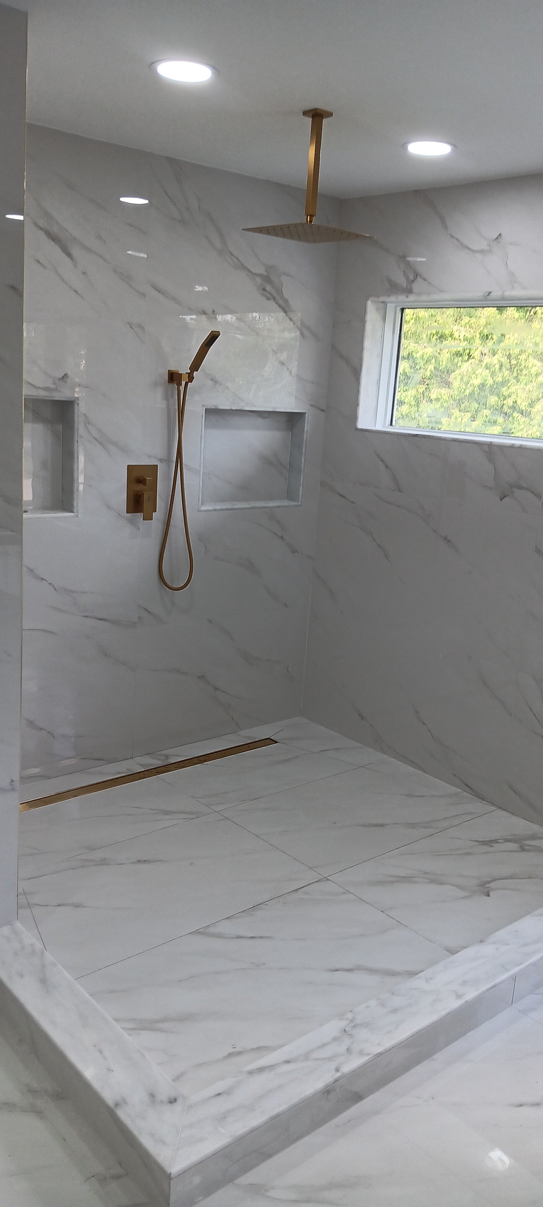 Completed walk-in shower featuring modern fixtures, built-in niches, glass panels, and bright natural light.