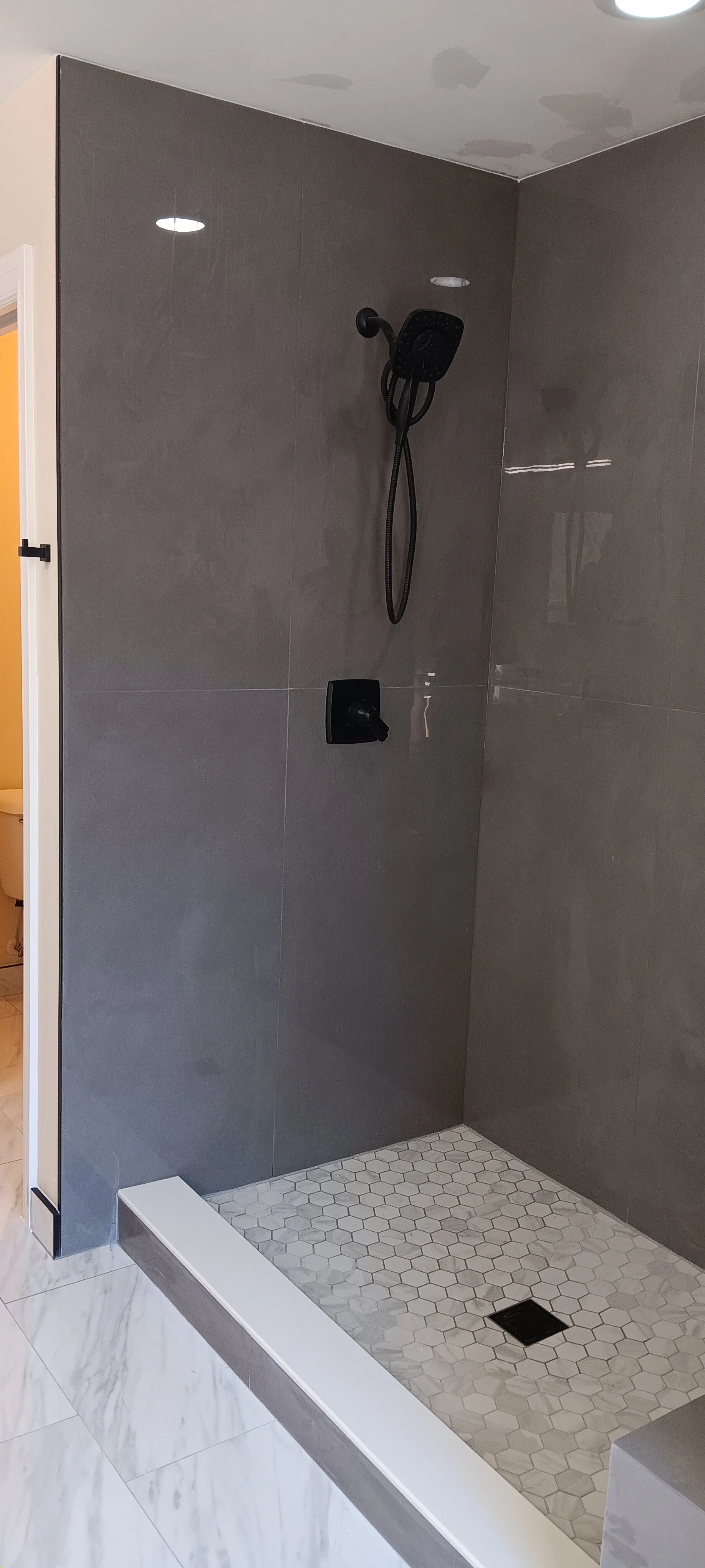 Modern walk-in shower with gray tile, built-in bench, recessed lighting, and matte-black fixtures.
