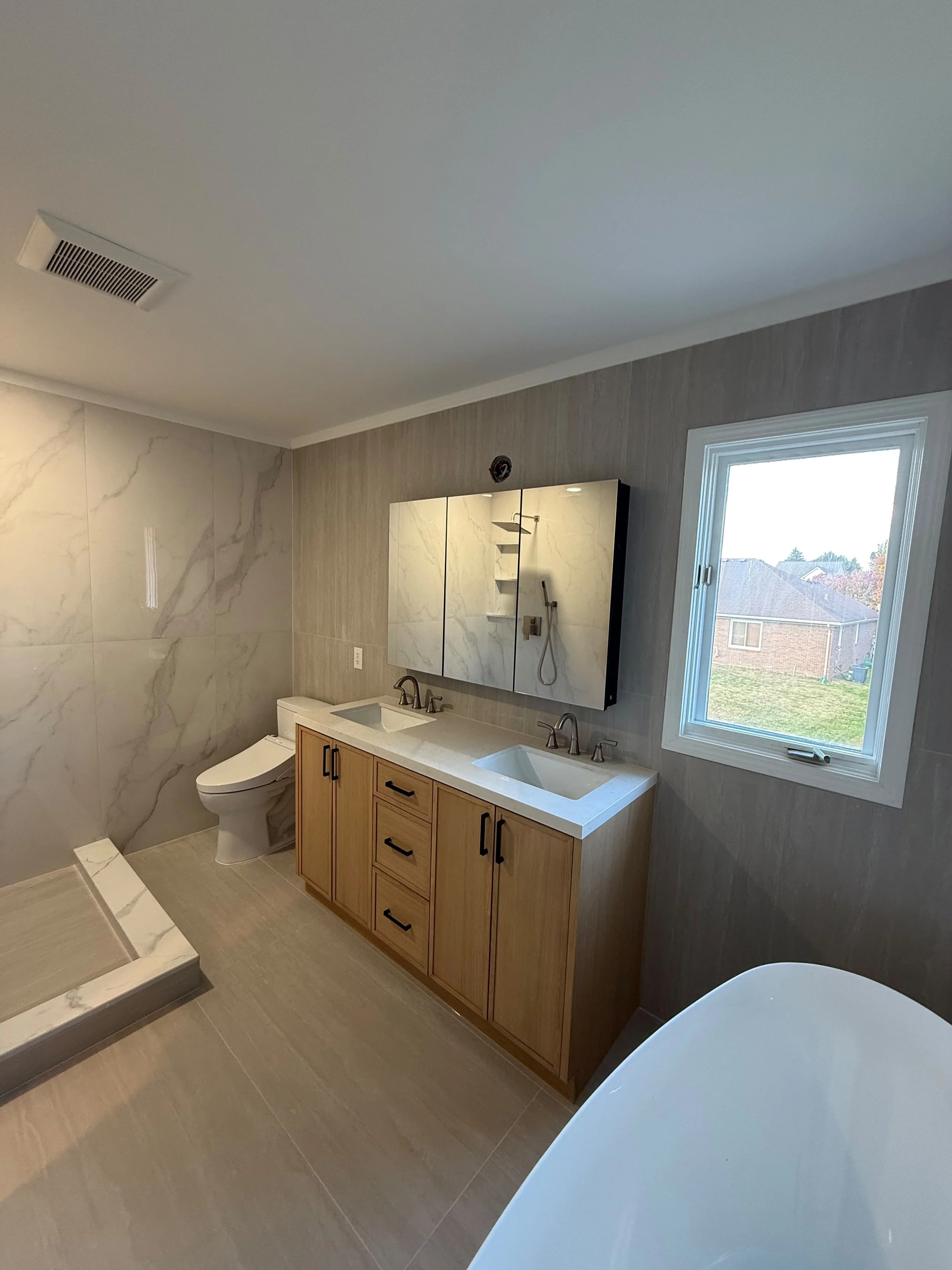 Modern bathroom remodel with wood vanity, quartz countertop, illuminated mirror, freestanding soaking tub, and custom finishes by Edilgjoni LLC in Rochester, Michigan.