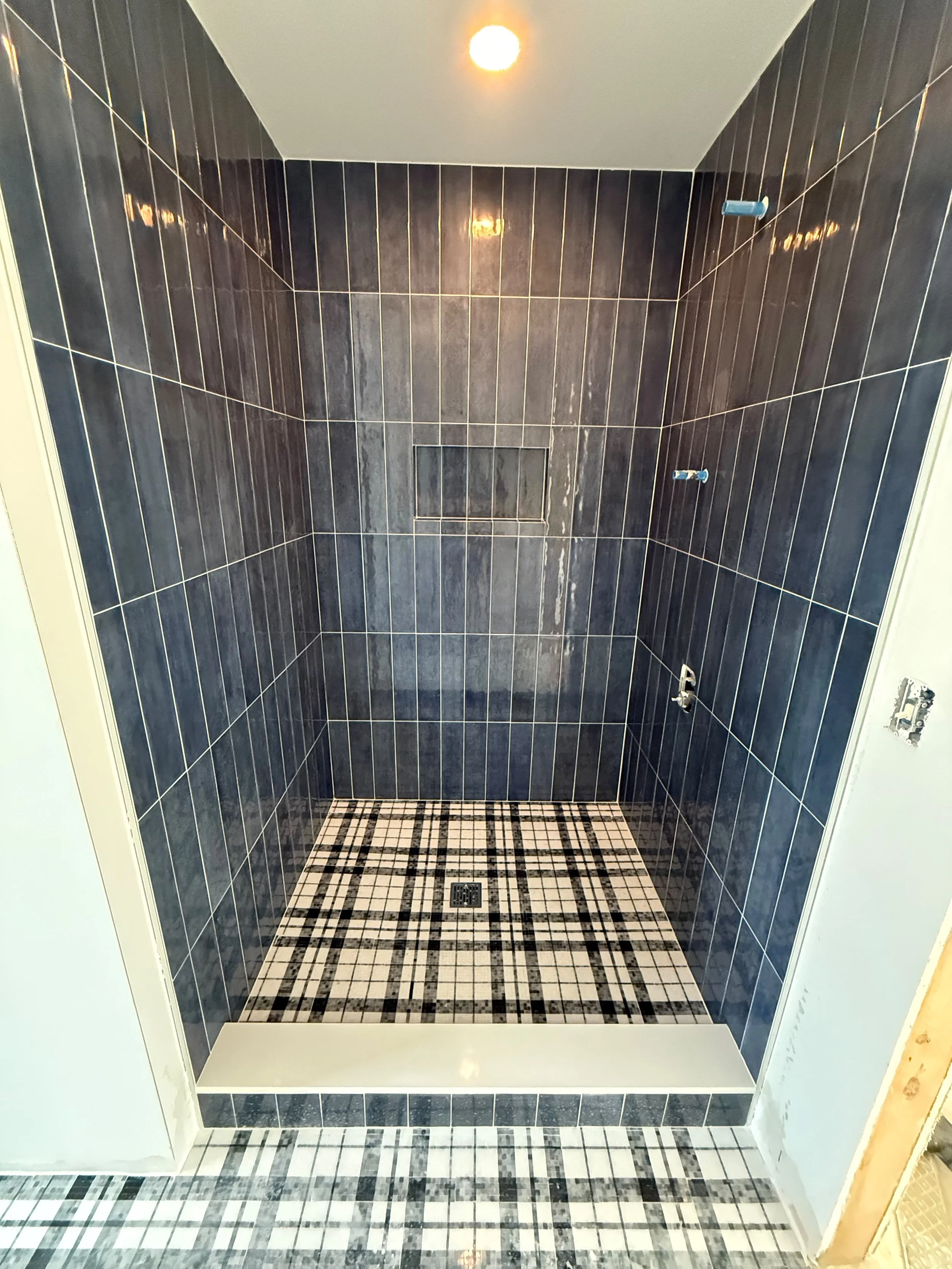 Luxury walk-in shower with sleek black tile walls, linear shower drain, custom recessed shelf, and decorative patterned tile flooring.