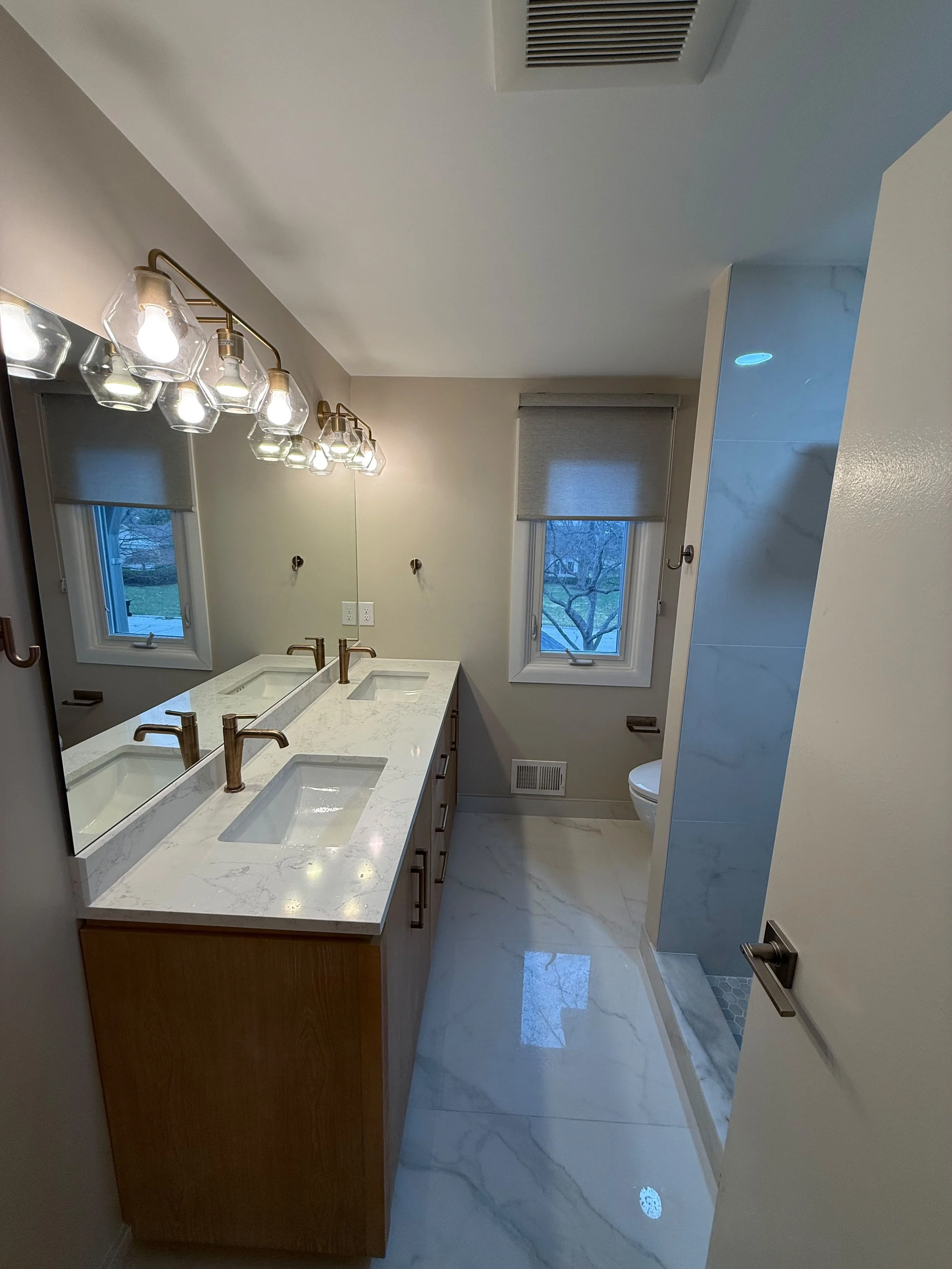 After bathroom renovation in Rochester , MI featuring a modern double vanity, luxury tile flooring, bright lighting, and a custom bathroom remodel by Edil Gjoni Remodeling.