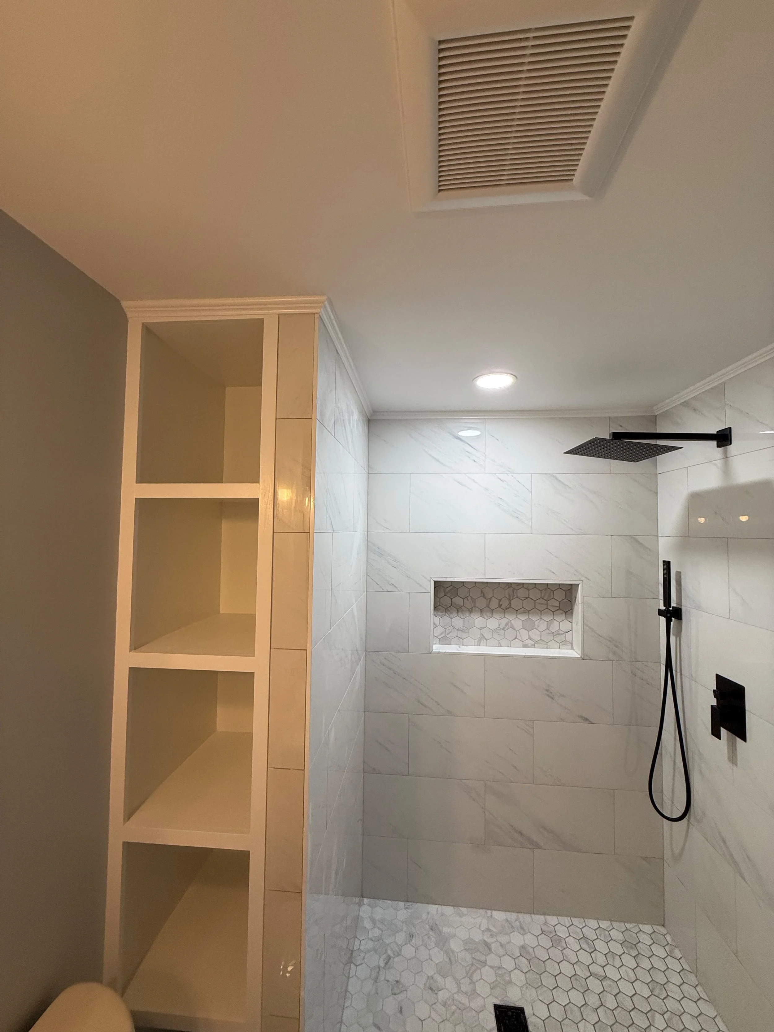 Finished custom walk-in shower with matte black rain shower fixture, recessed wall niche, pebble mosaic floor, and open-concept design in a Rochester bathroom in Rochester , MI by Edil Gjoni LLC