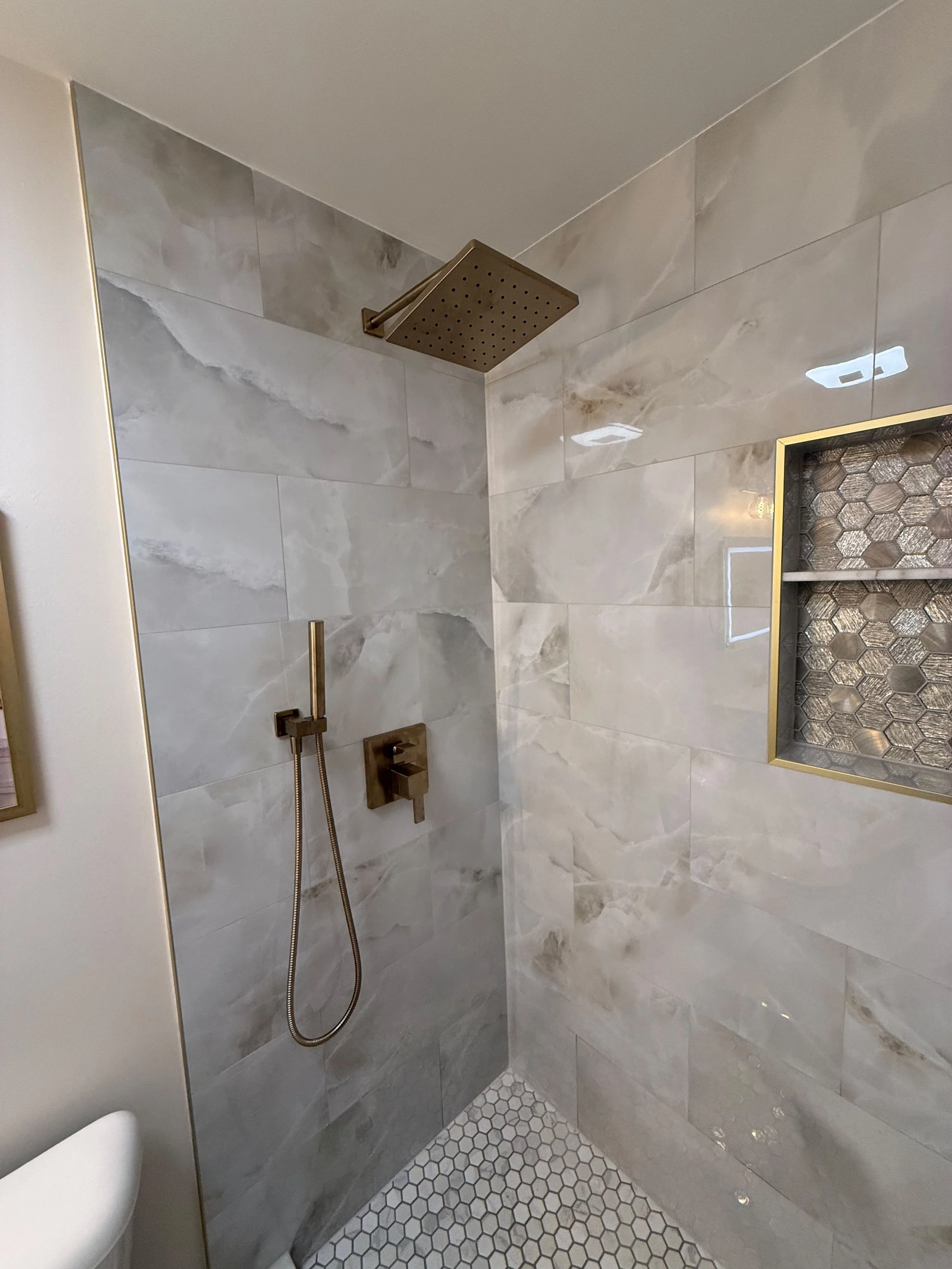 Walk-in shower featuring large gray porcelain wall tile, a matte black rainfall shower system, recessed storage niche, and pebble mosaic shower floor.