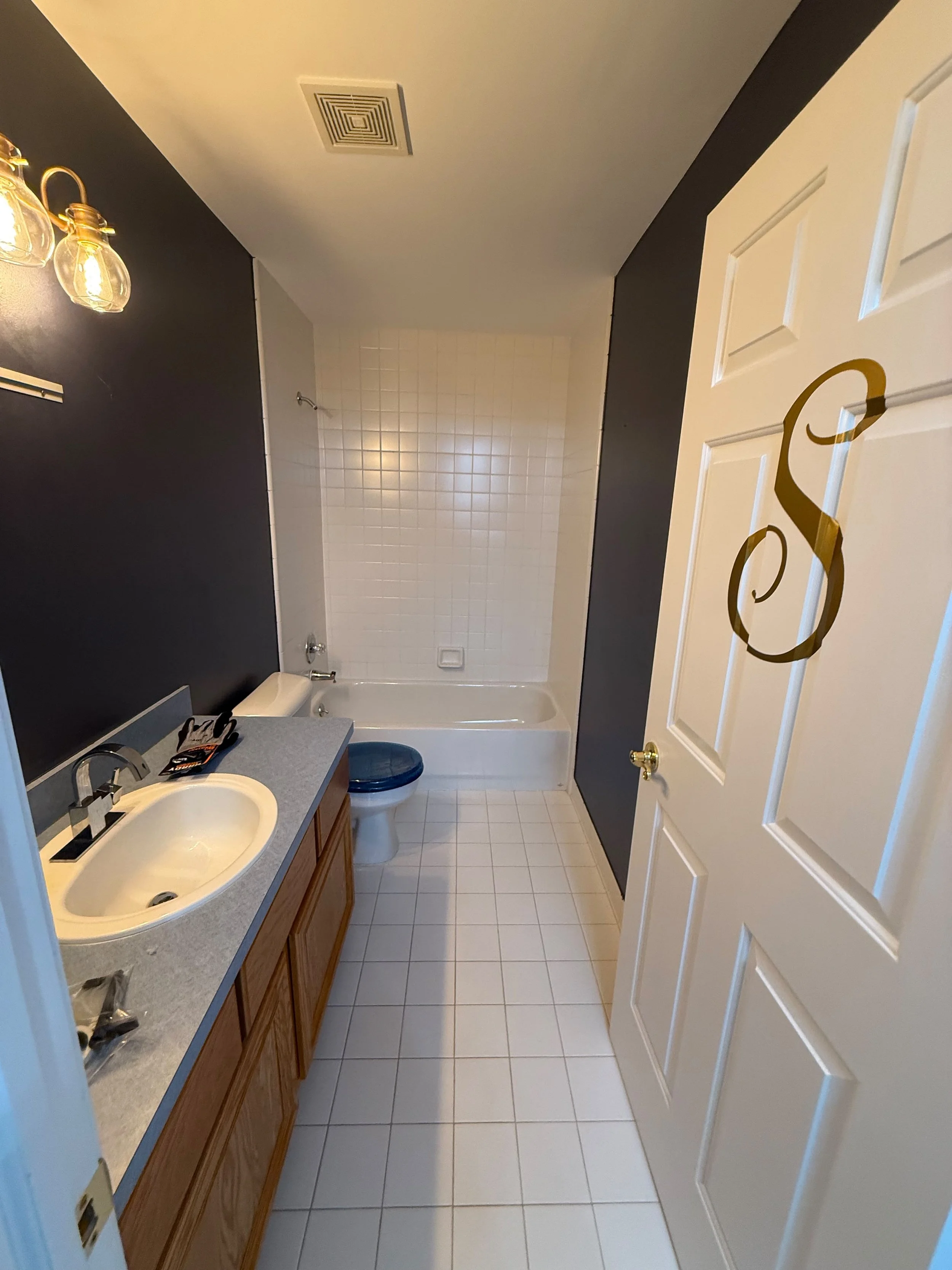 Narrow bathroom layout featuring a single-sink vanity, full-length tile flooring, dark accent wall, and a bright, functional design leading to the shower area.