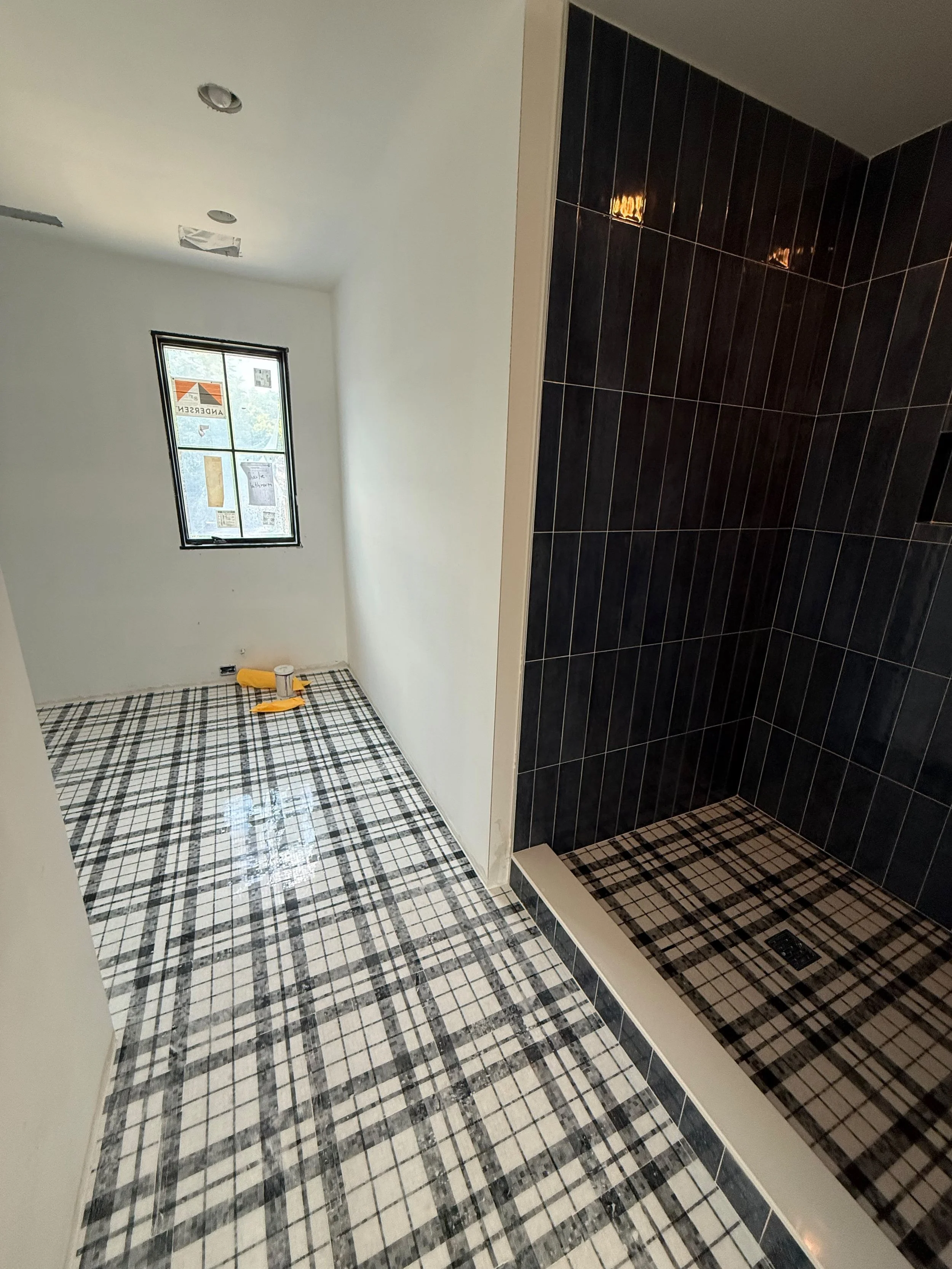 Spacious bathroom with eye-catching checkered porcelain flooring, a large window for natural light, and a custom shower positioned at the end of the room.