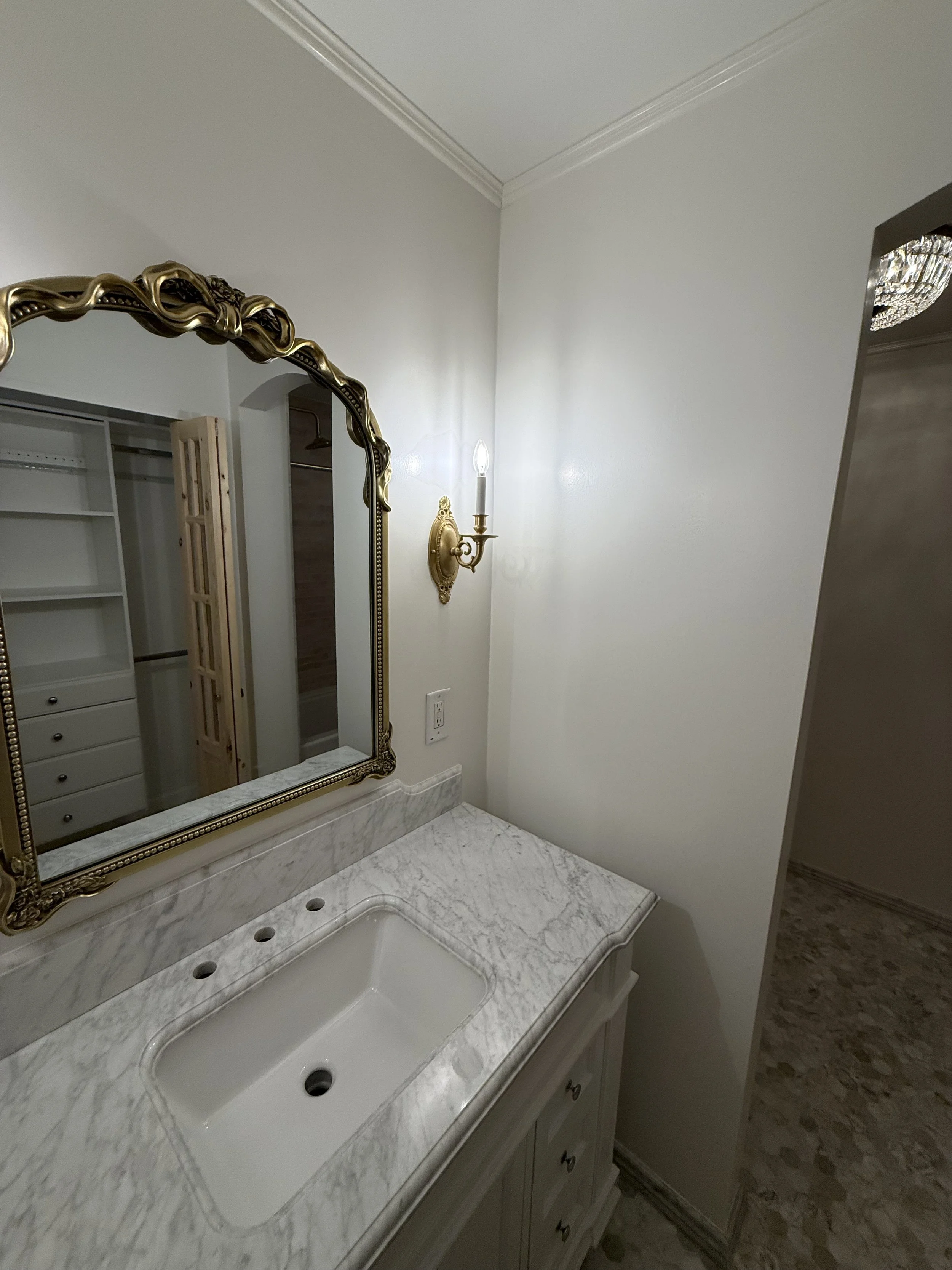 Bathroom vanity with a white countertop, framed mirror, wall lighting, and detailed mosaic flooring.