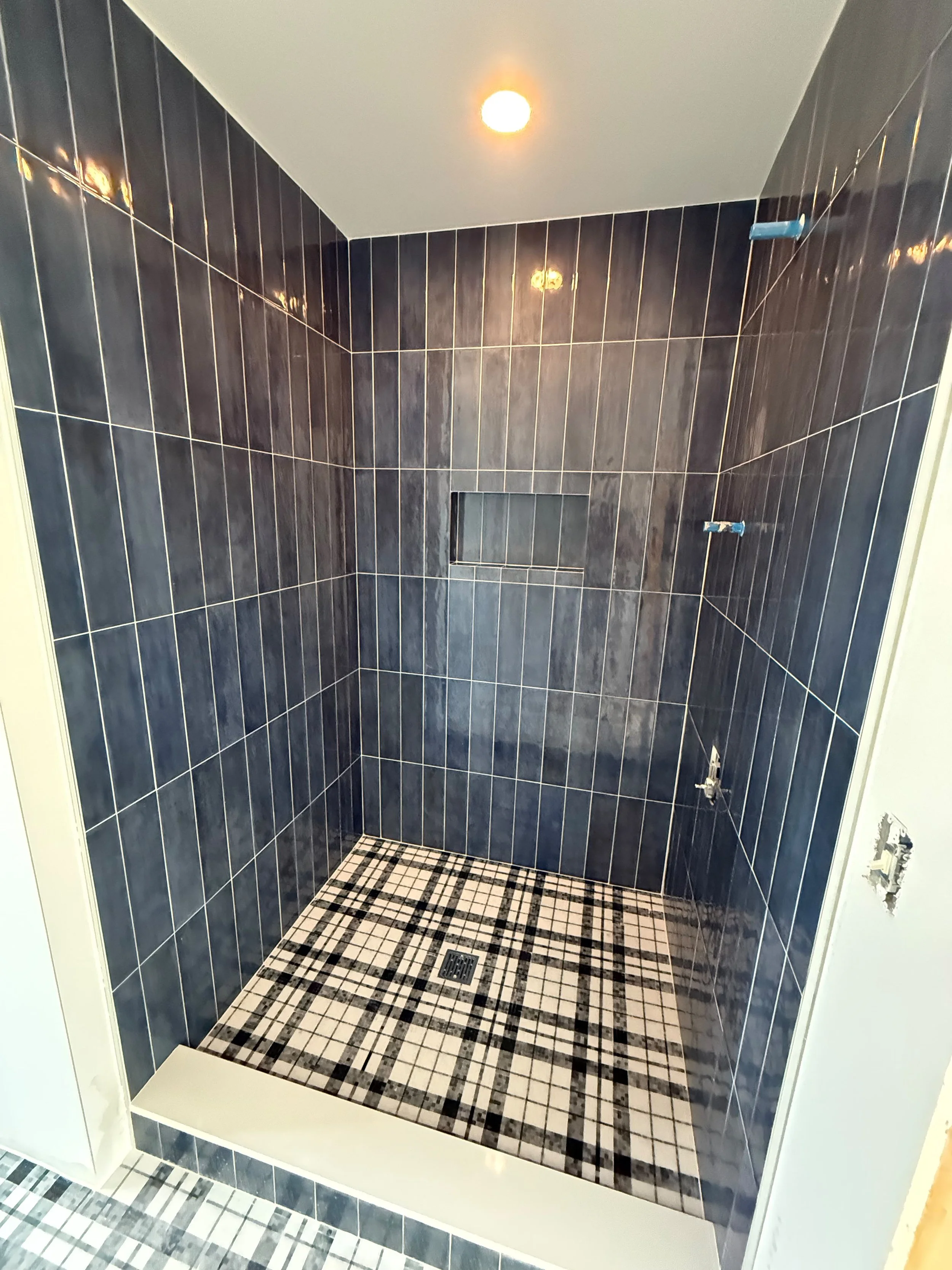Angled view of a luxury walk-in shower featuring black ceramic wall tile, a built-in floor tile, and clean contemporary finishes.
