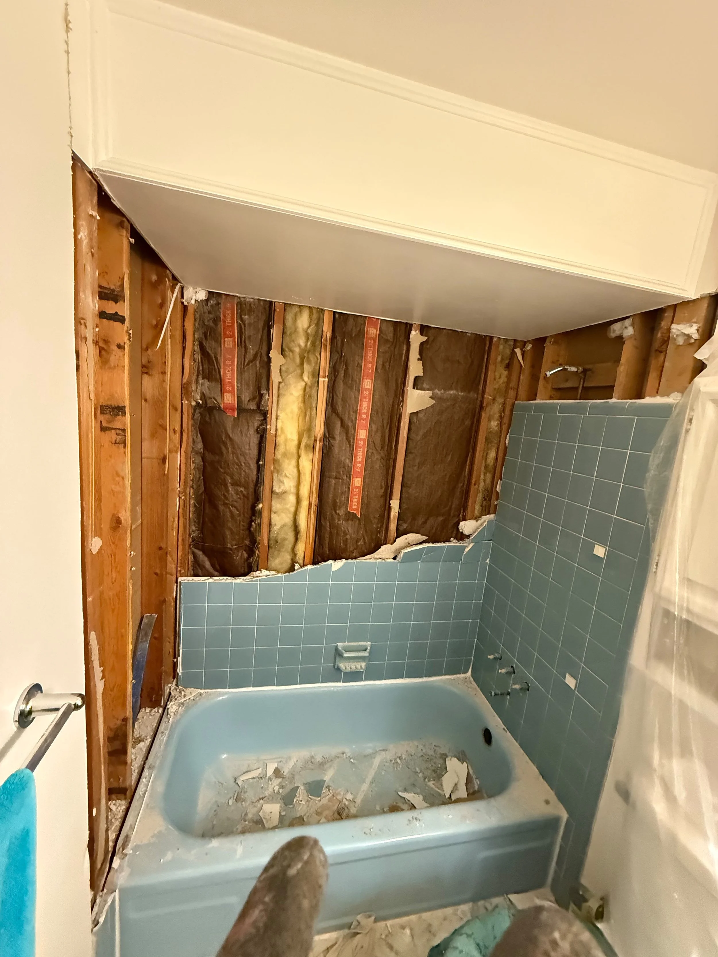 Outdated bathroom before renovation with exposed wall framing , an original blue bathtub, and demolition in progress before the remodel.