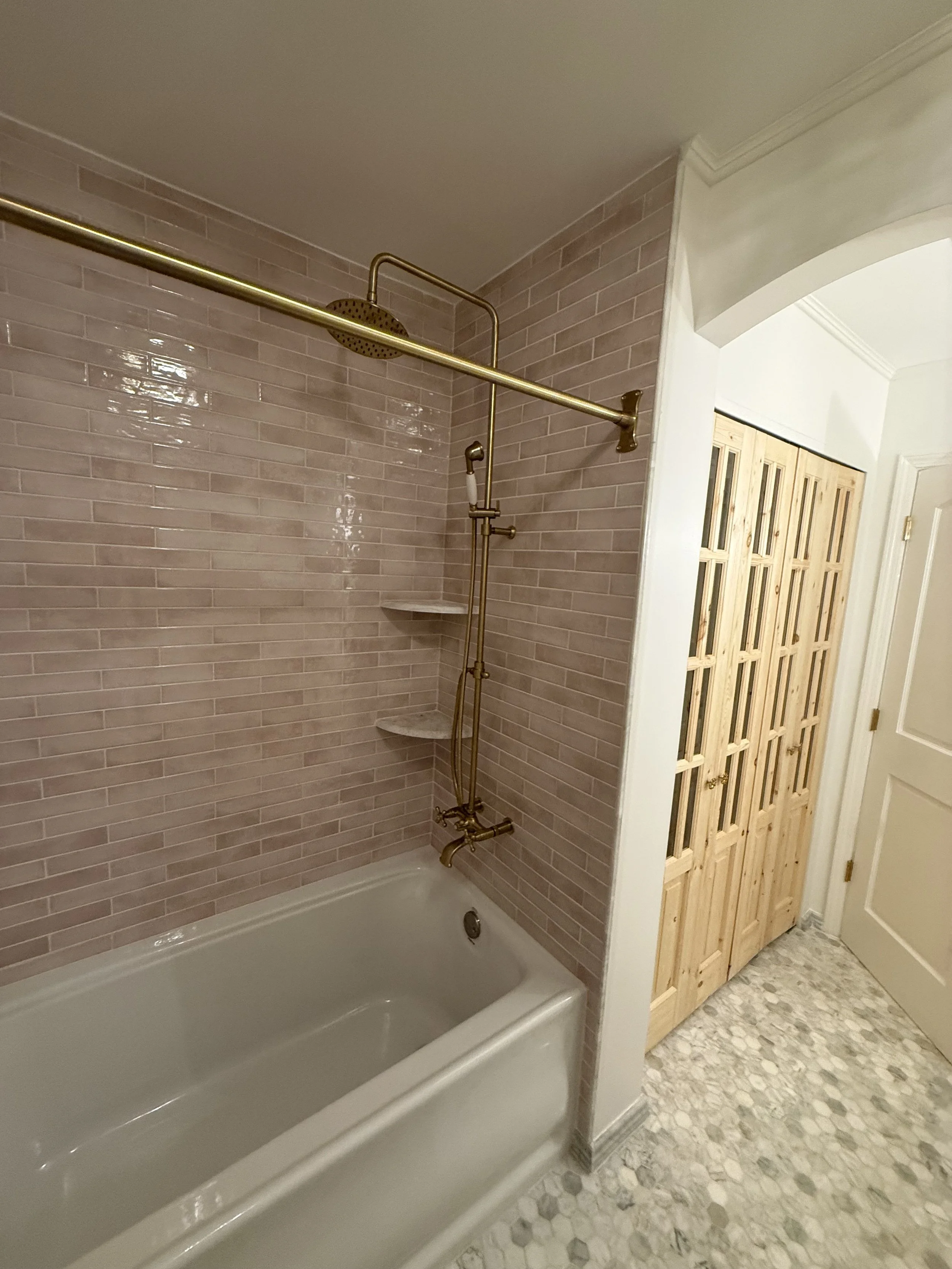 Renovated bathtub and shower area with large gray wall tiles beside a natural wood bathroom door.