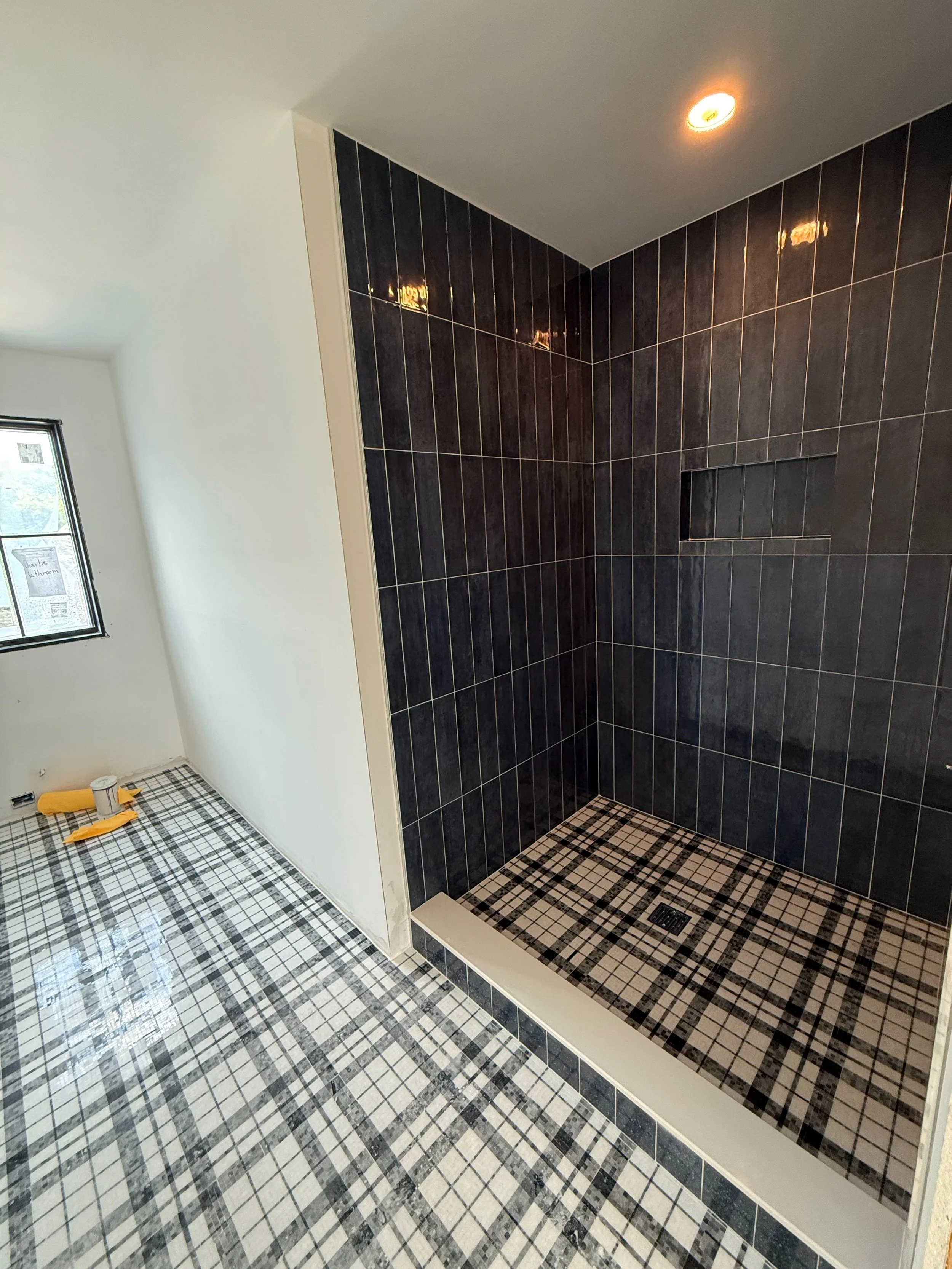 Custom walk-in shower featuring glossy black wall tile, a recessed storage niche, and bold plaid-pattern porcelain floor tile in Deaborn, MI.