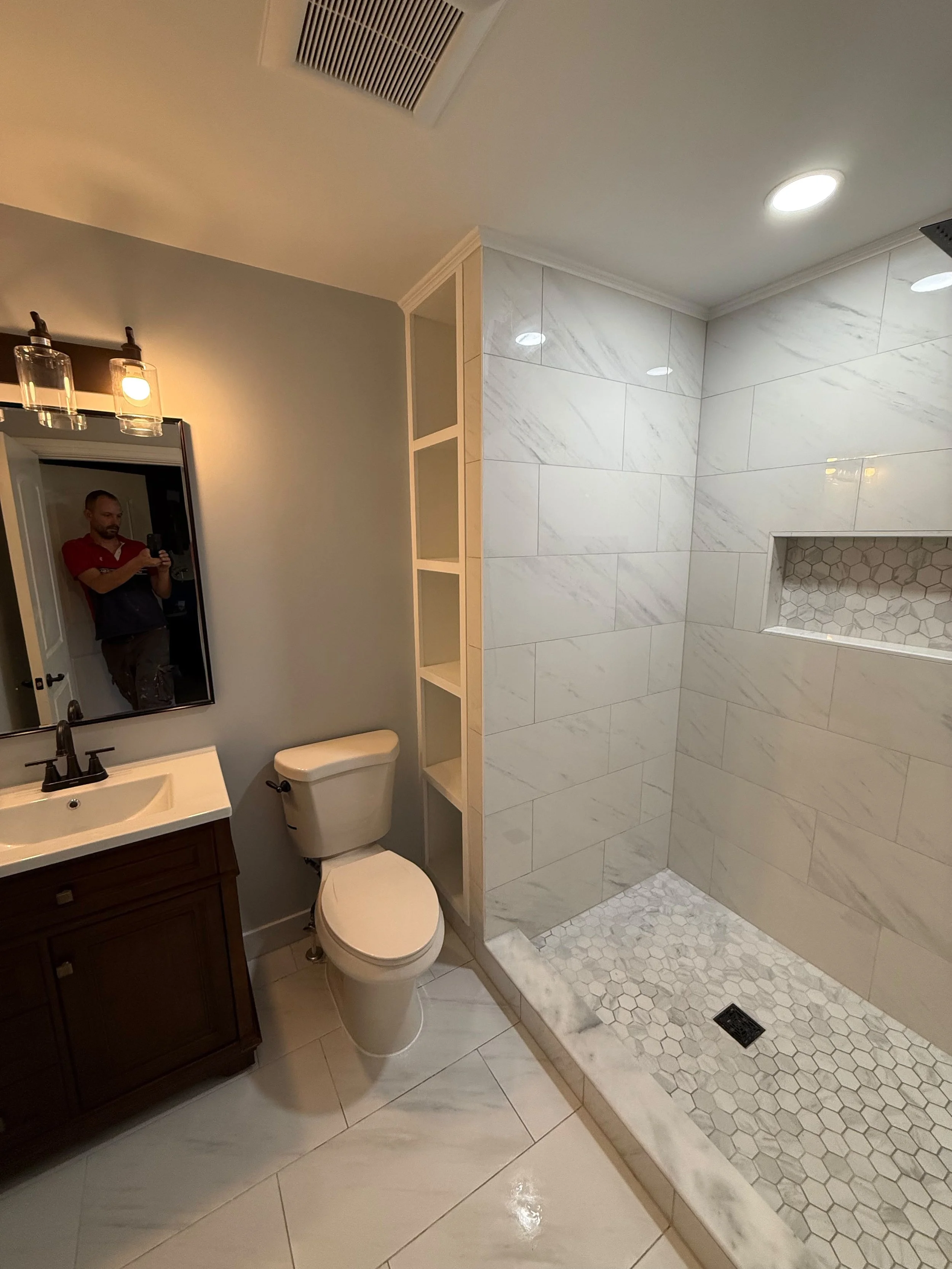 Open-concept bathroom showcasing a curbless walk-in shower with a built-in wall niche, custom storage shelving, modern vanity, and coordinated gray tile throughout the space.