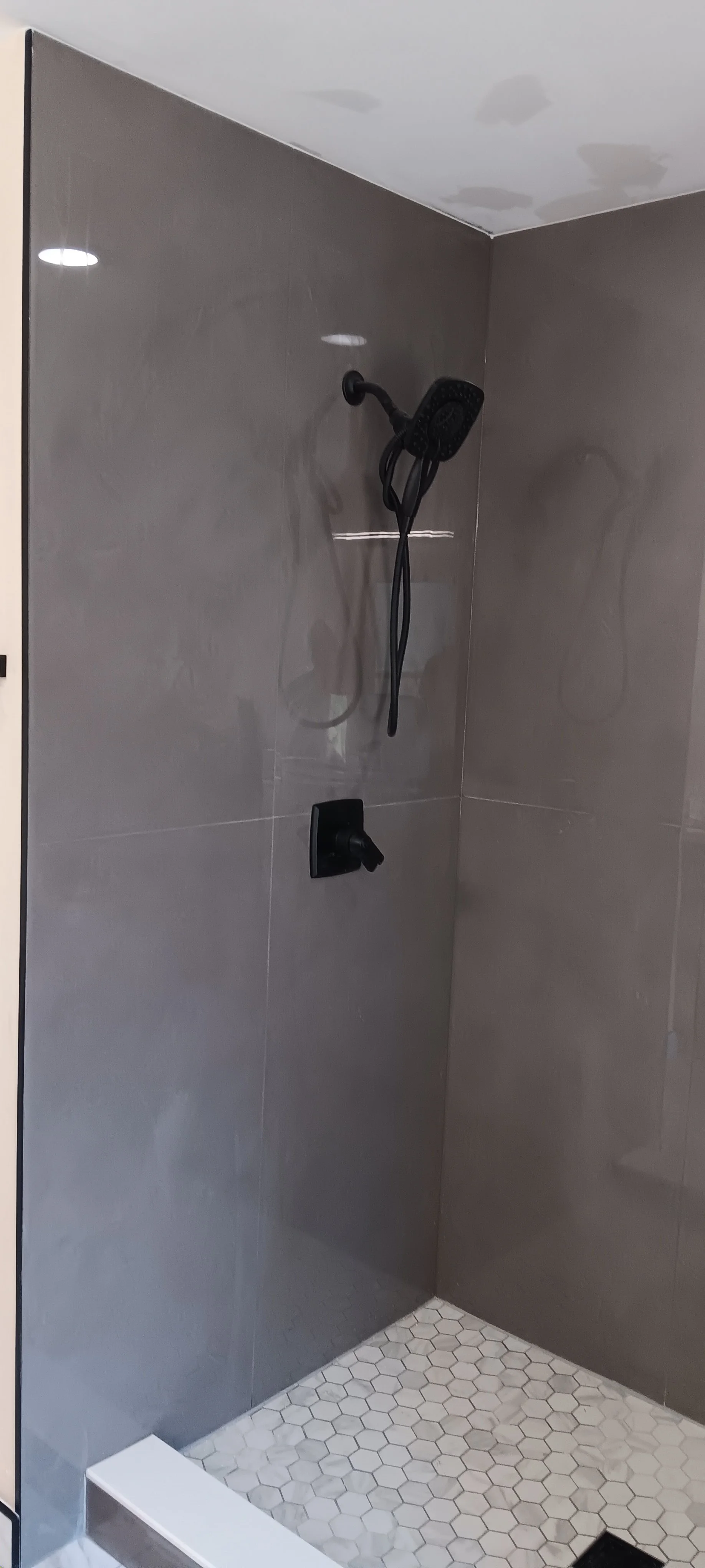 Custom walk-in shower featuring modern tile, a built-in bench, recessed lighting, and matte-black fixtures.