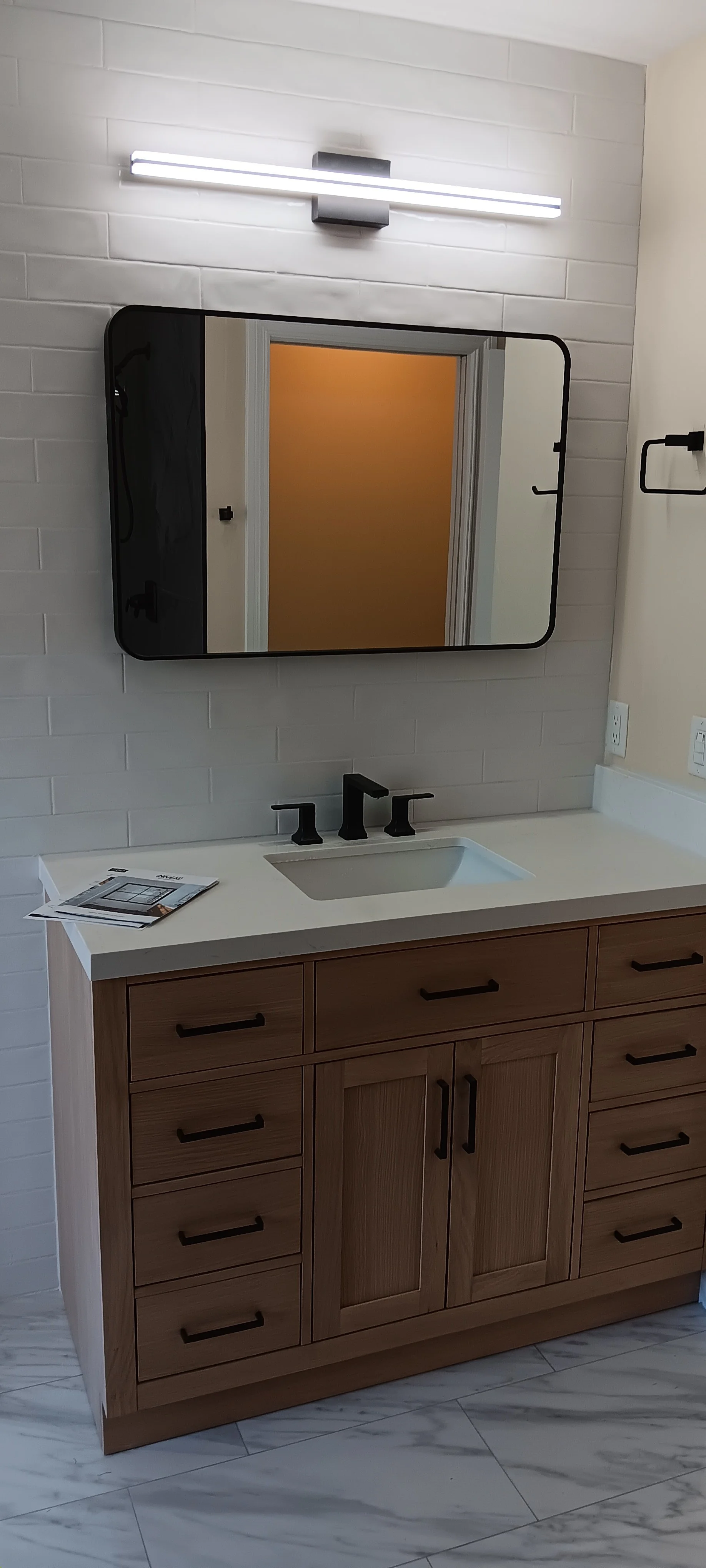 Modern bathroom vanity with custom gray cabinetry, white countertop, black fixtures, framed mirror, and contemporary lighting.