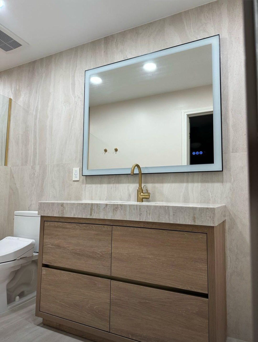 The oversized illuminated mirror and custom vanity create a bright, elegant focal point while maximizing both style and functionality.