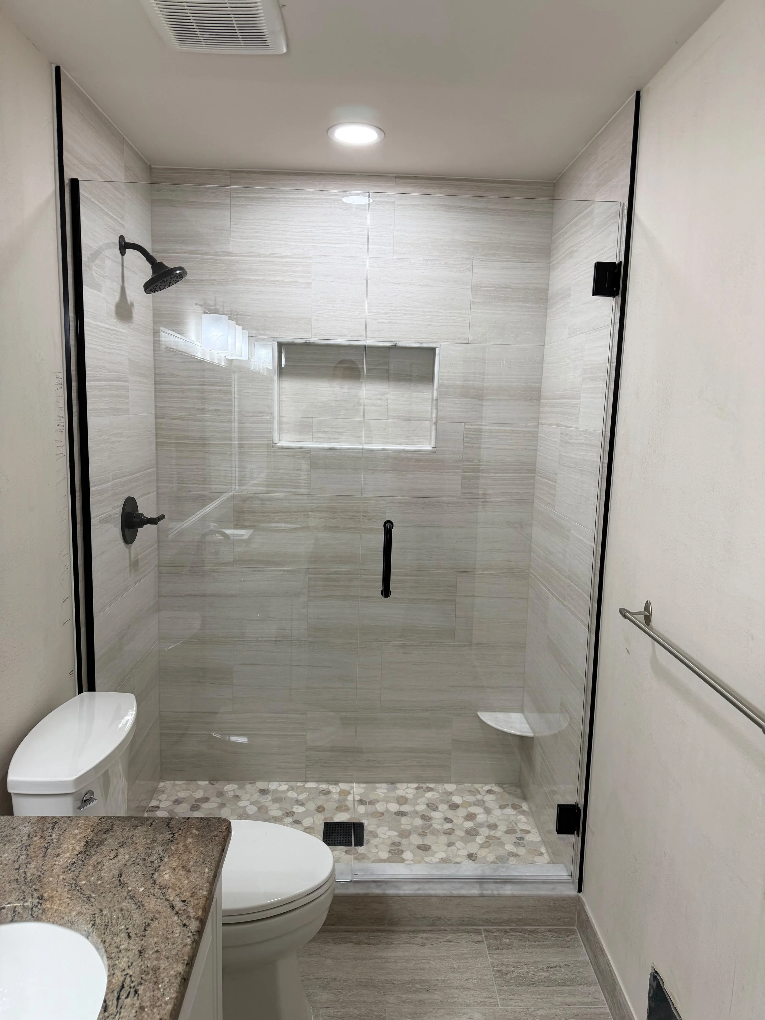 Modern bathroom remodel featuring a frameless glass shower, custom white tile walls, built-in shower niche, black fixtures, and premium flooring by Edilgjoni LLC in Southeast Michigan.