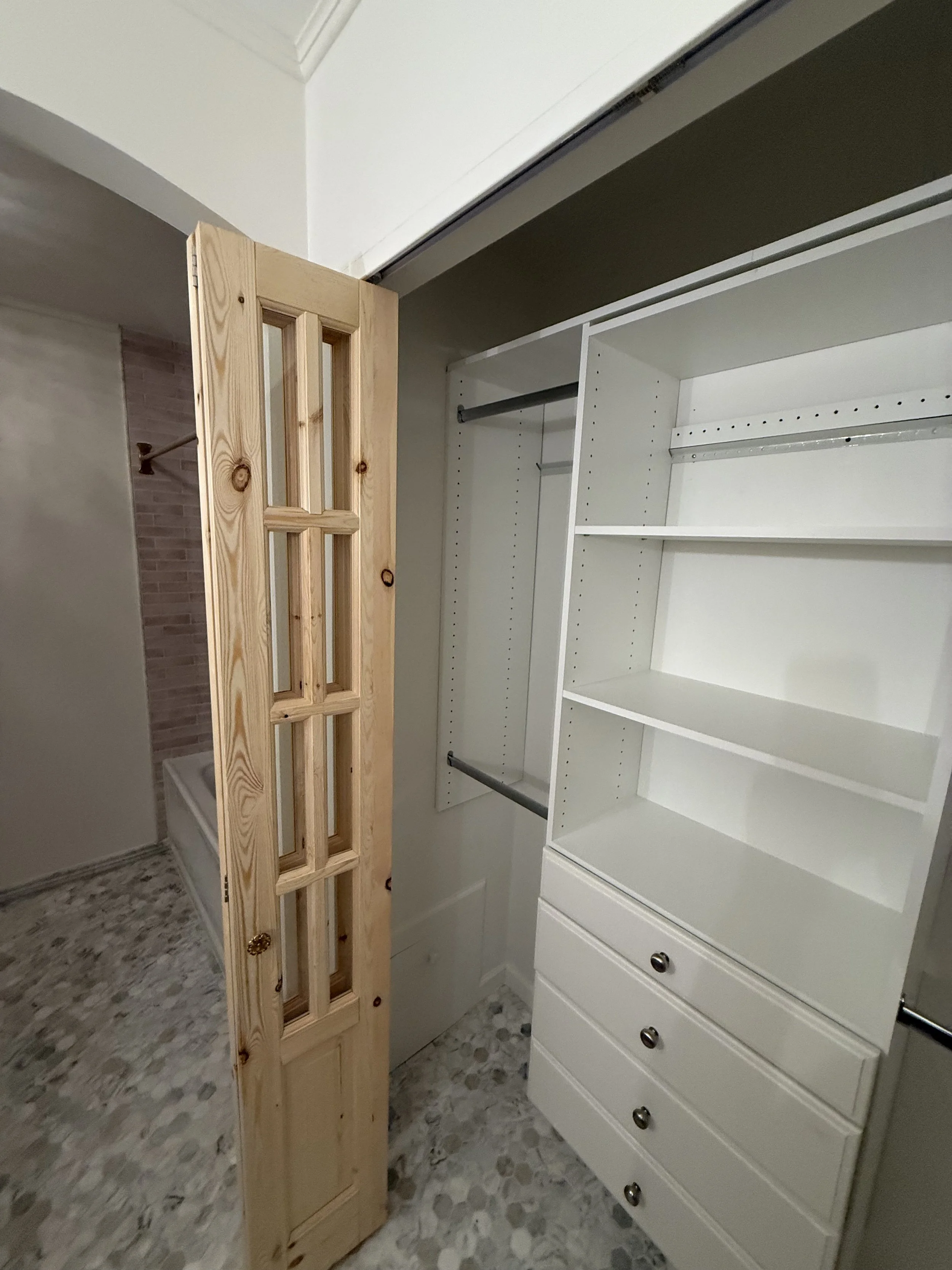 Custom white built-in bathroom shelving installed beside a natural wood glass-panel door.