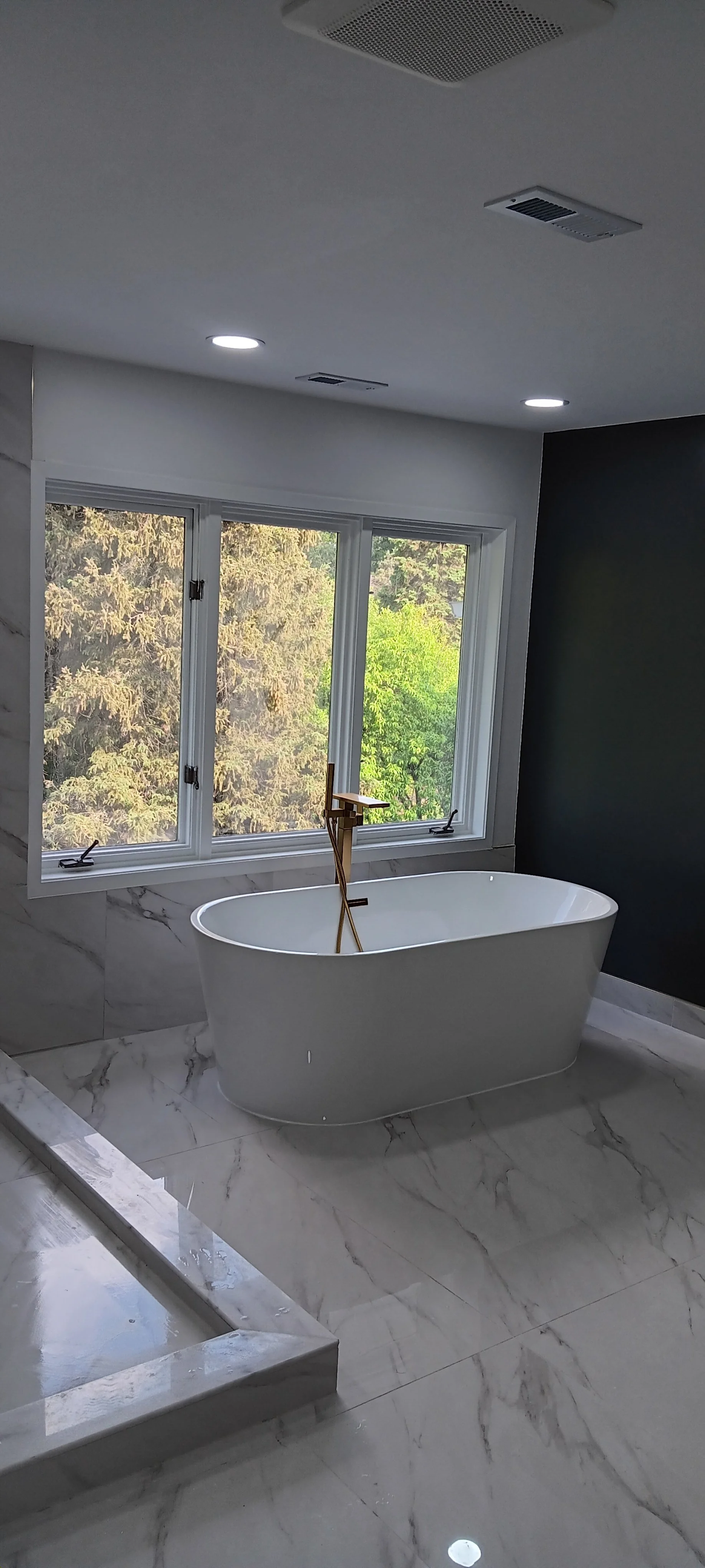 Modern freestanding bathtub positioned beneath large windows for natural light and a relaxing view.
