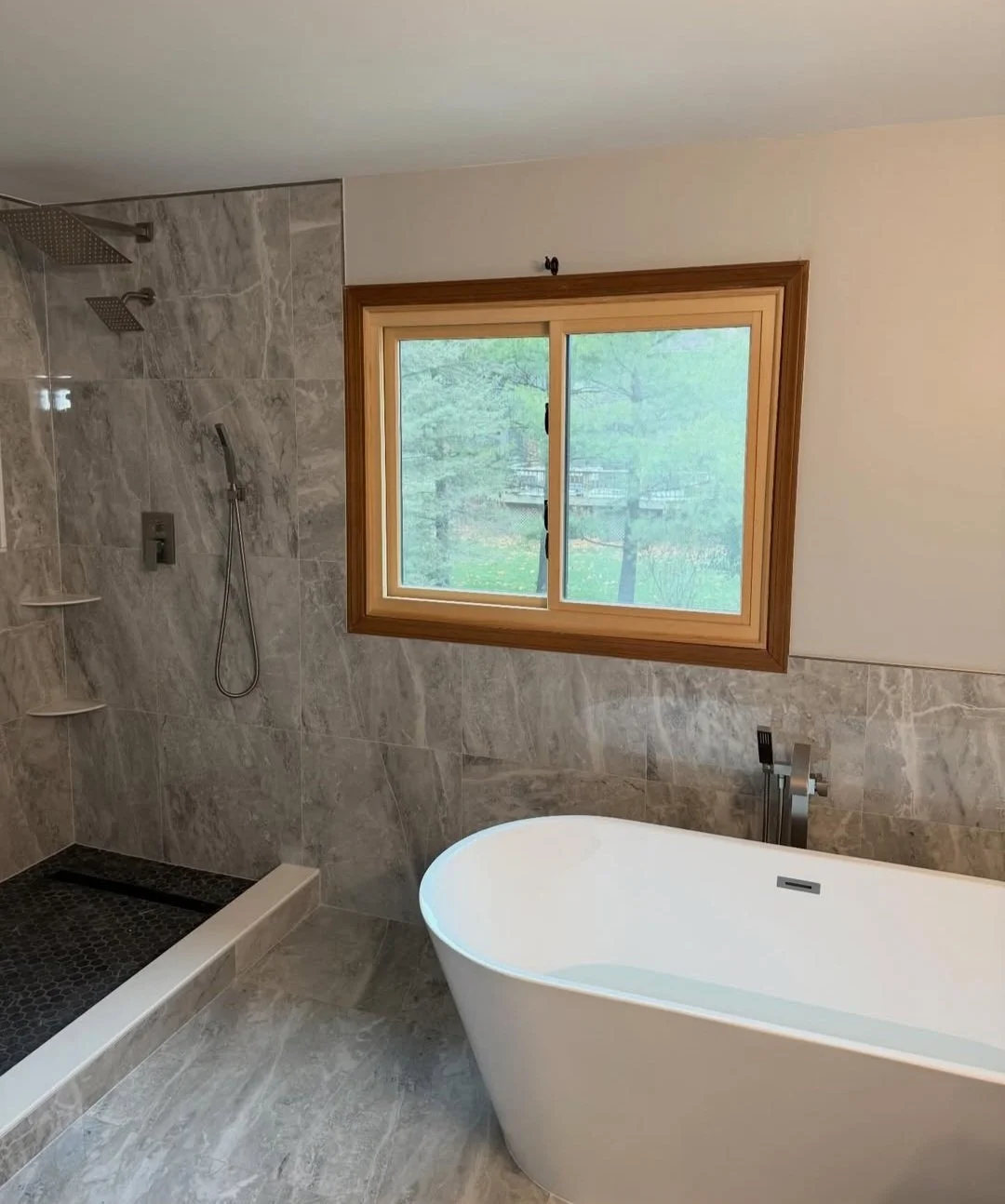 A modern bathroom with a frosted window, a freestanding bathtub, and a shower area with gray marble tiles.