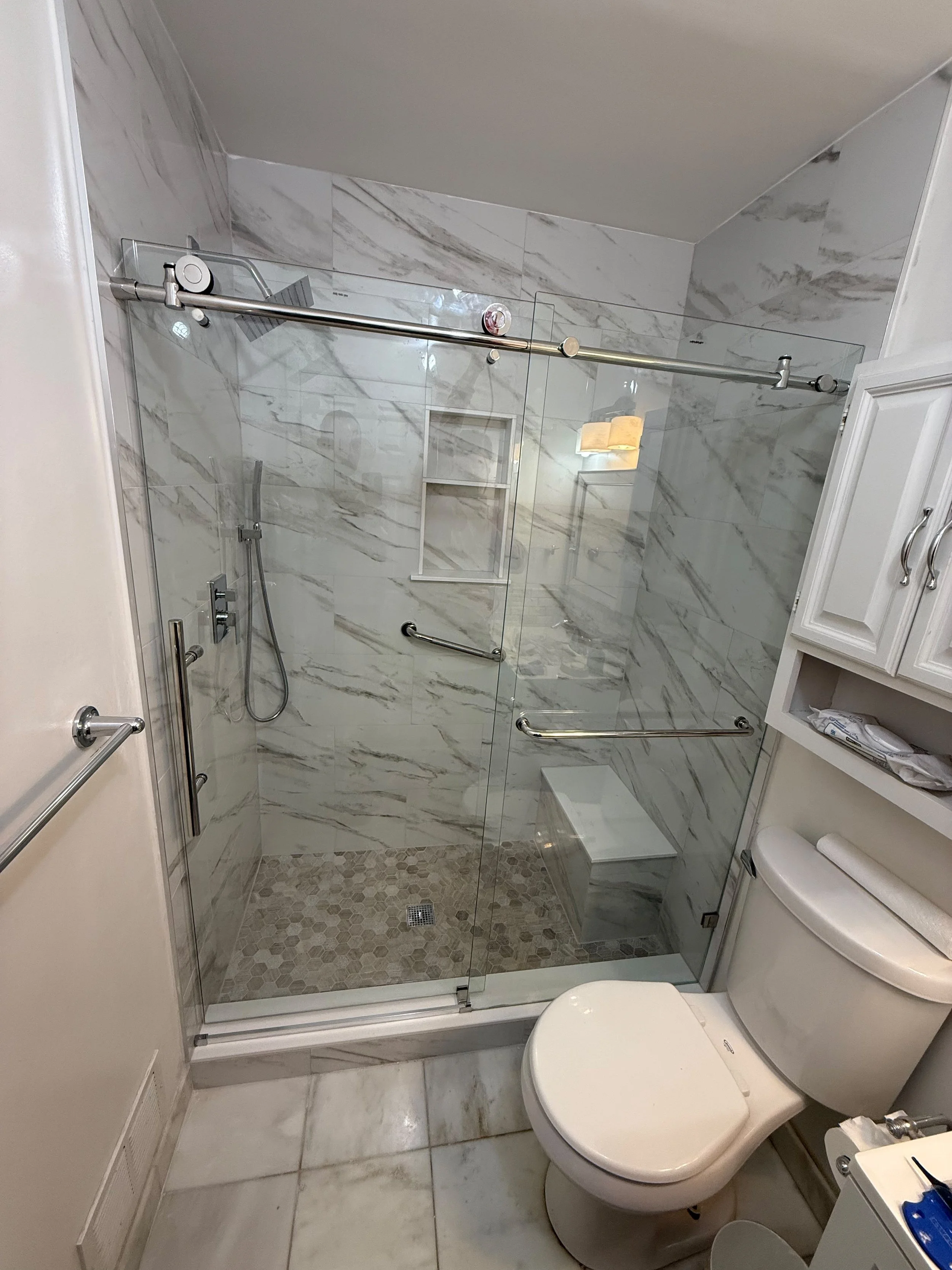 Bright bathroom featuring a frameless glass shower enclosure, marble-look wall tile, built-in shower bench, and an efficient layout with modern fixtures.