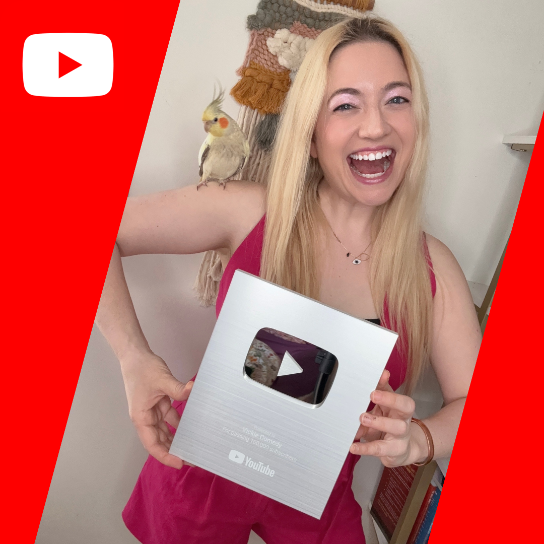 A woman with long blonde hair smiling and holding a YouTube Silver Play Button award, with a cockatiel perched on her shoulder, inside a room.