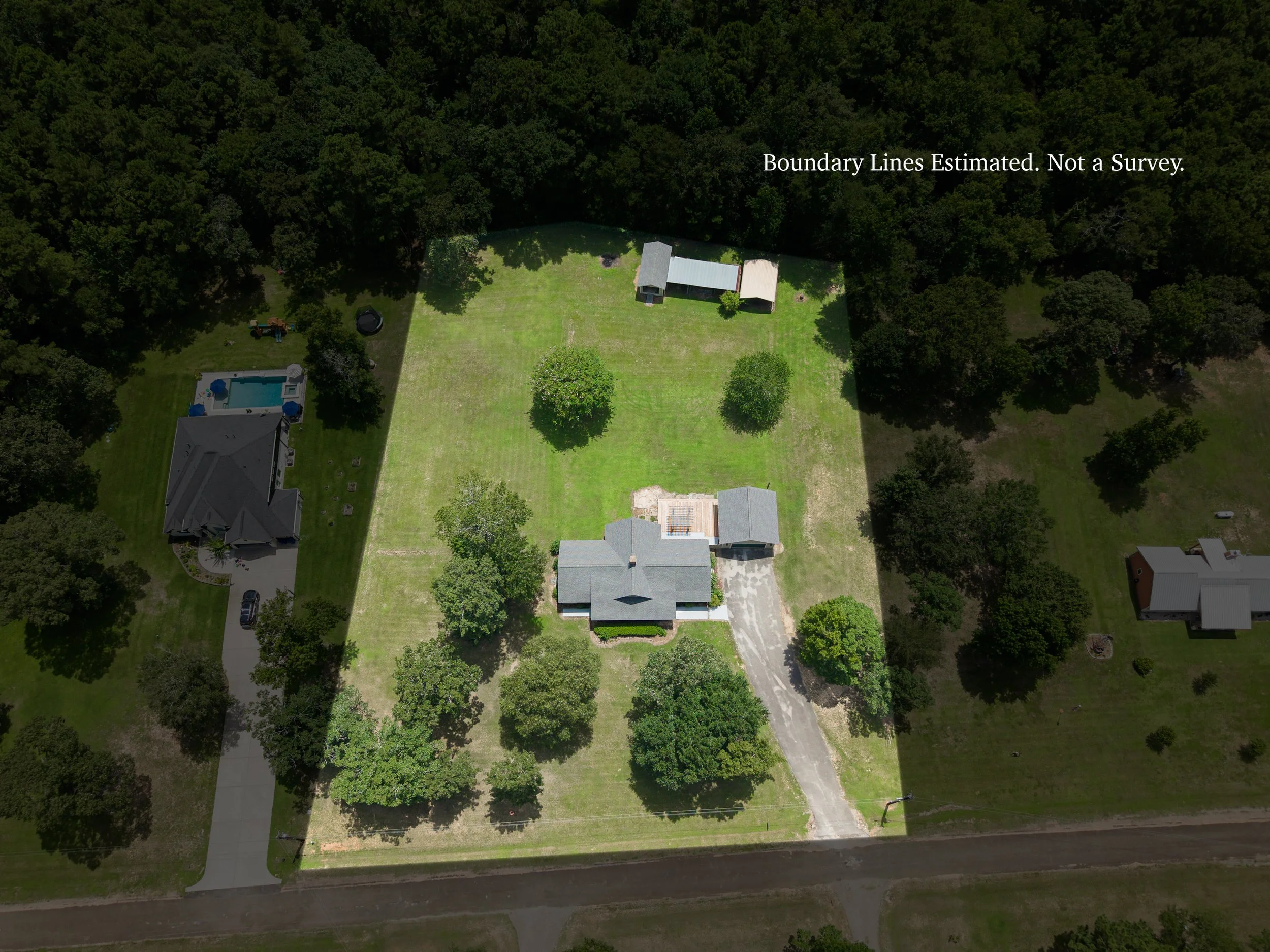 An aerial view of a residential backyard with a house, yard, and surrounding trees, with a disclaimer about boundary lines.