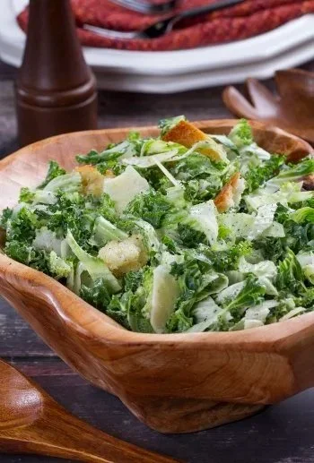 Caesar salad with romaine lettuce, croutons, and shaved Parmesan cheese in a wooden bowl.