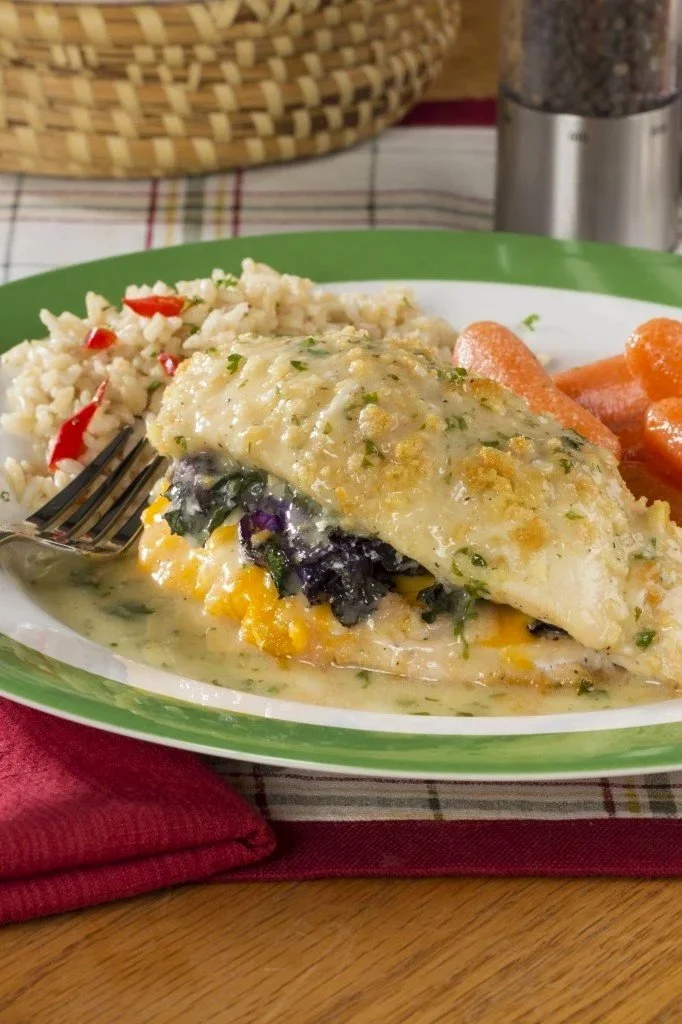 A plate of baked fish topped with creamy sauce, served with rice pilaf and cooked carrots in a household setting.